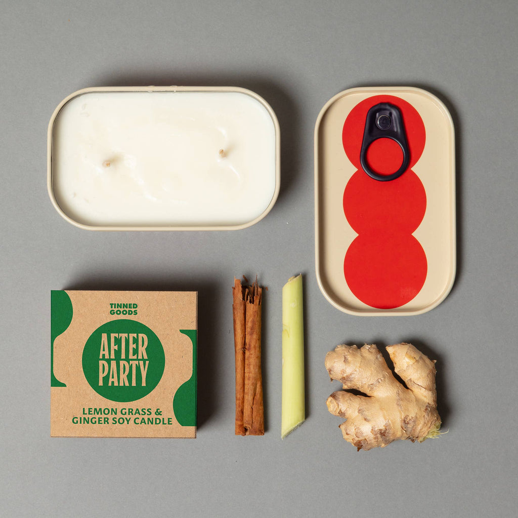 Candle, packaging, cinnamon sticks, ginger root, and a red and beige container on a gray background