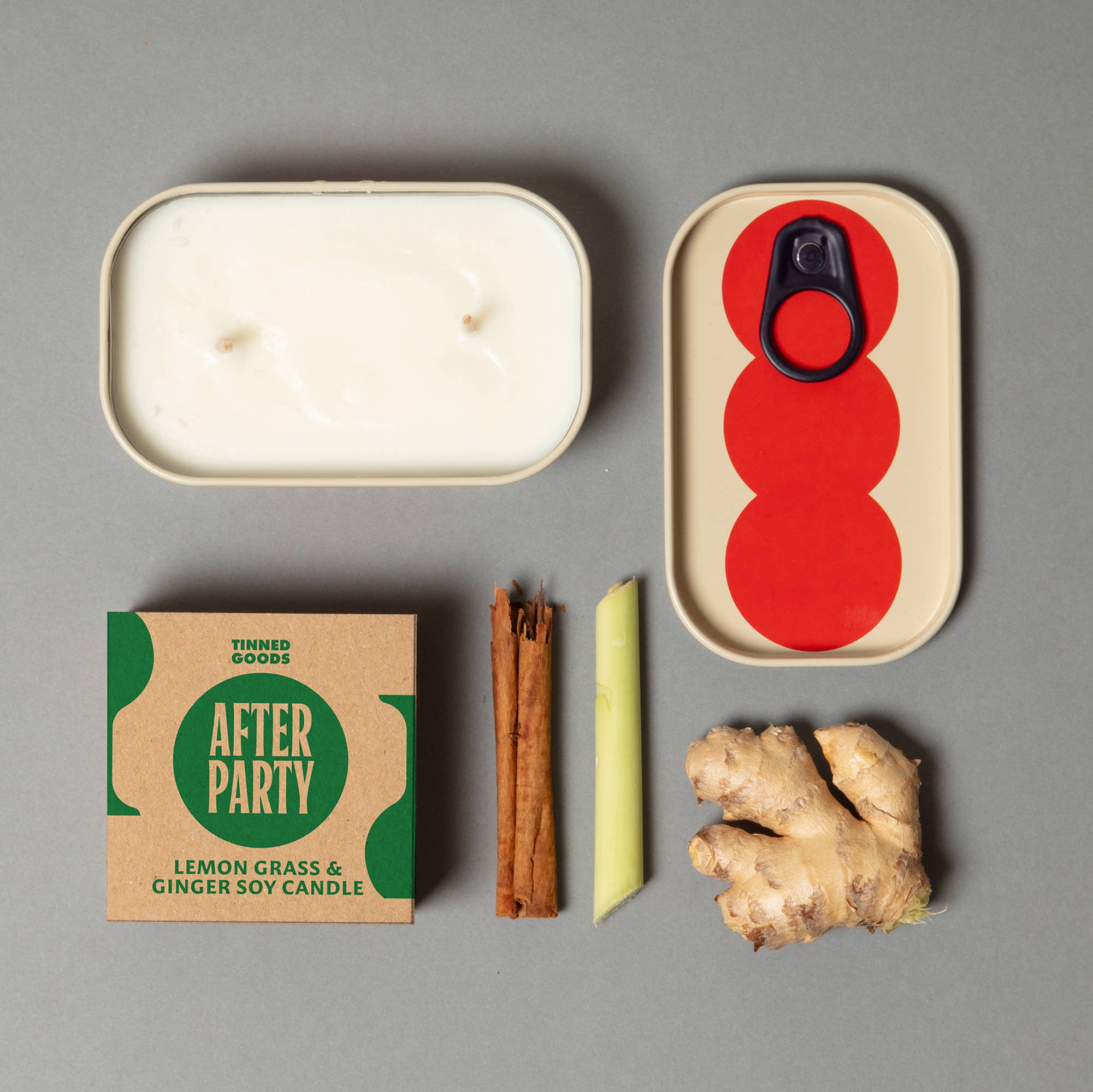 Candle, packaging, cinnamon sticks, ginger root, and a red and beige container on a gray background