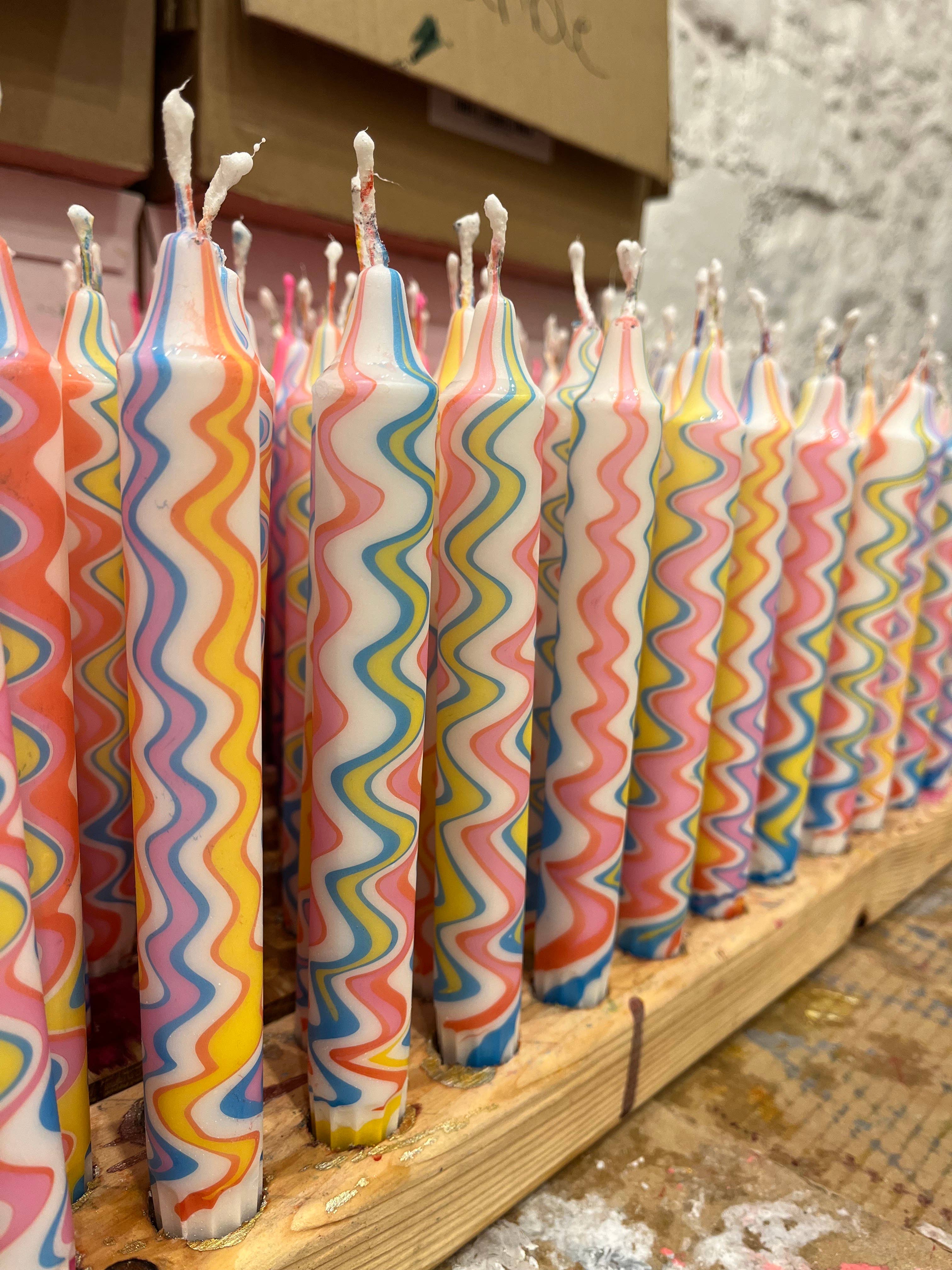 Colorful wavy-patterned candles on a wooden board with a blurred background.