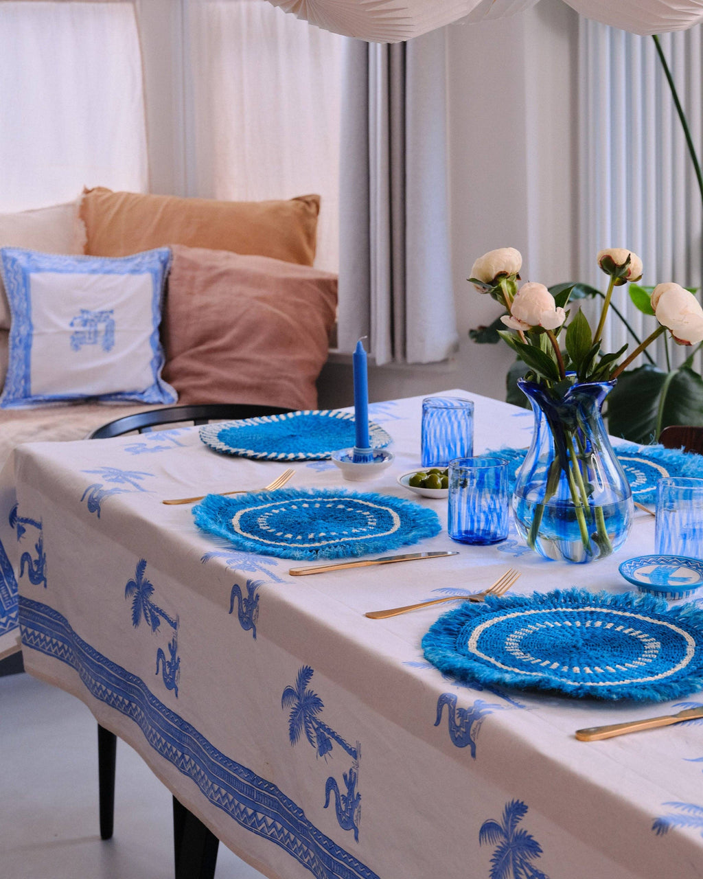 Dining table set with blue and white tablecloth, plates, and decor in a modern living room.