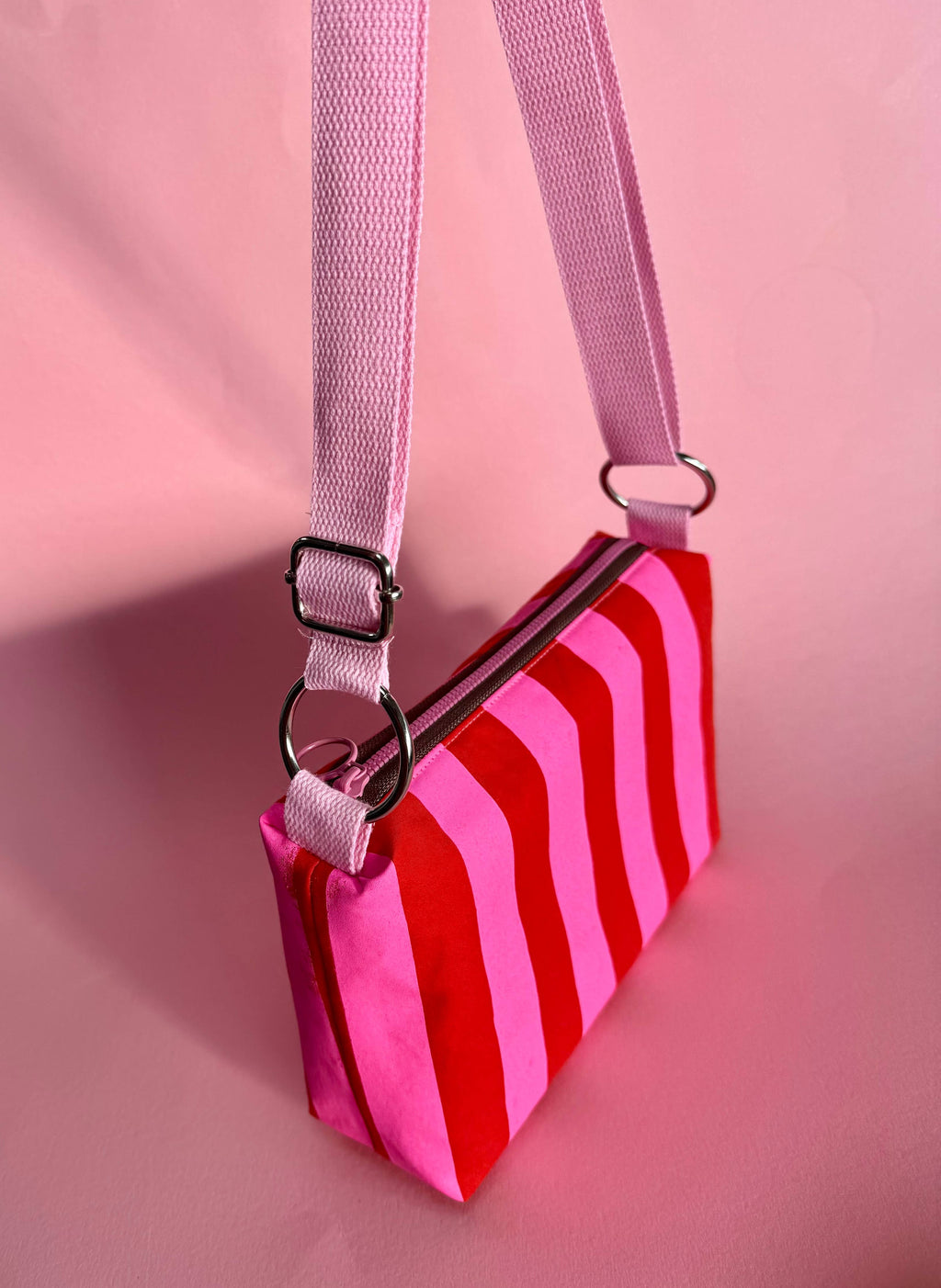 Pink and red striped bag with a pink strap on a pink background