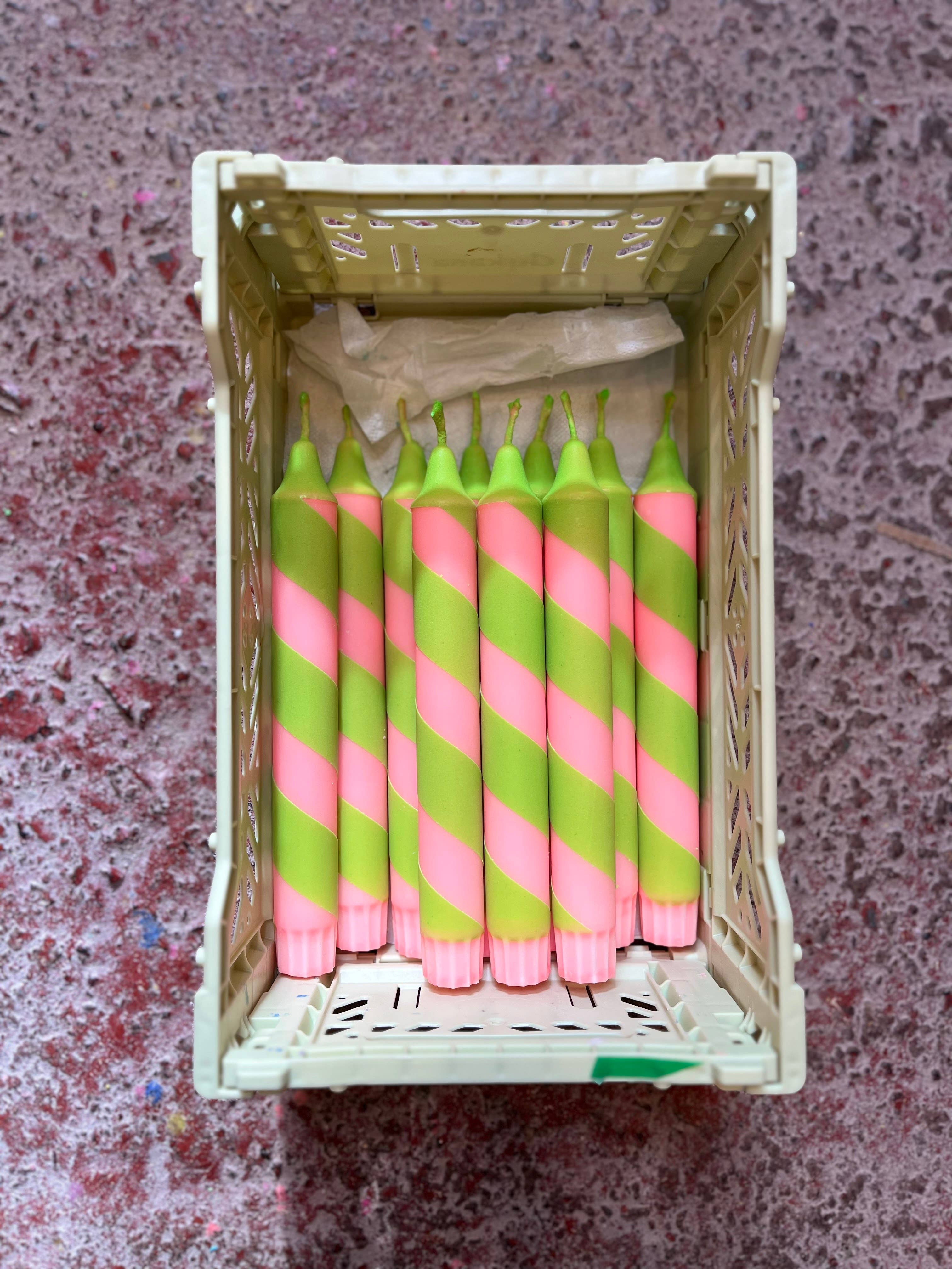 Box with pink and green striped candles on a textured surface