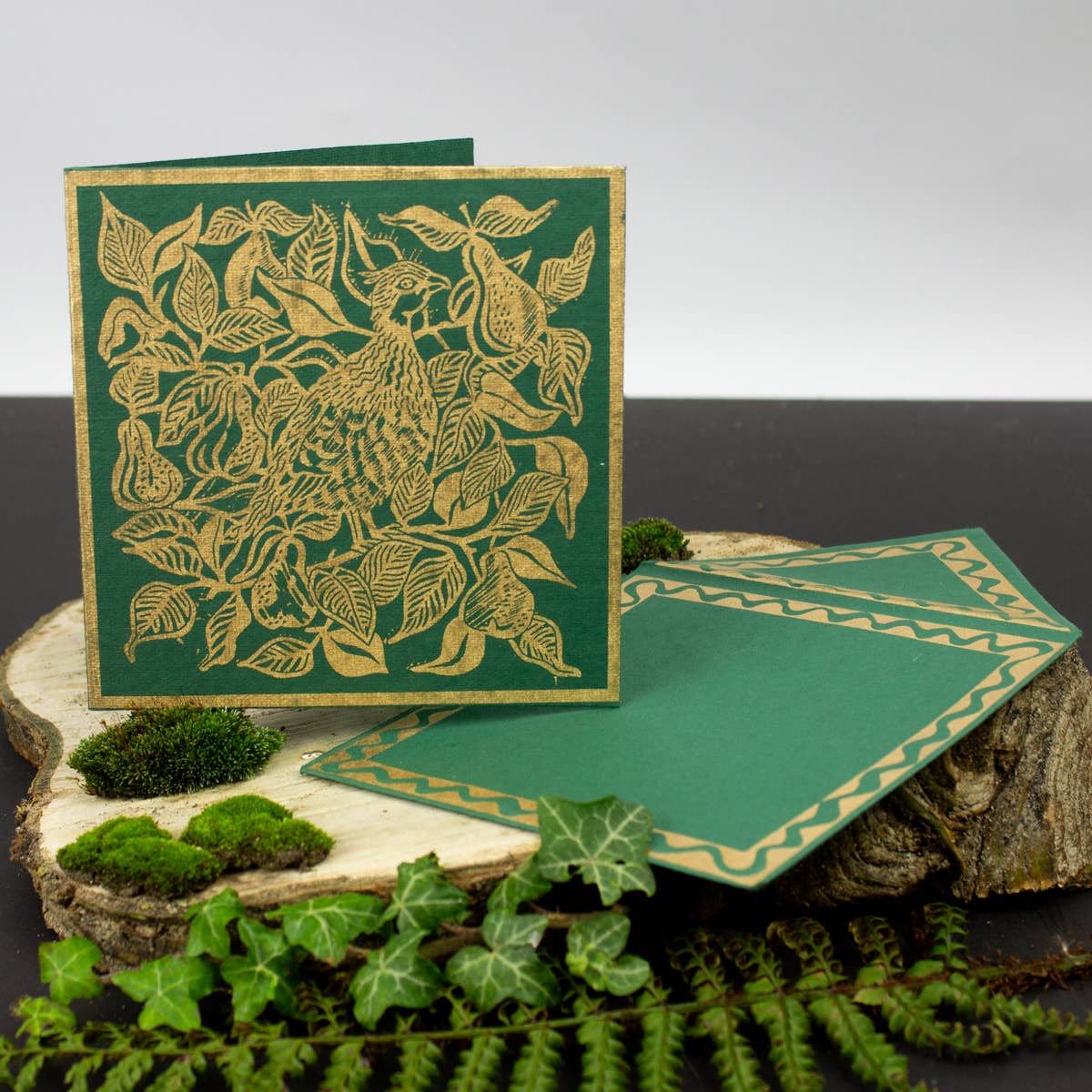 Green card with gold leaf design on a wooden surface with greenery