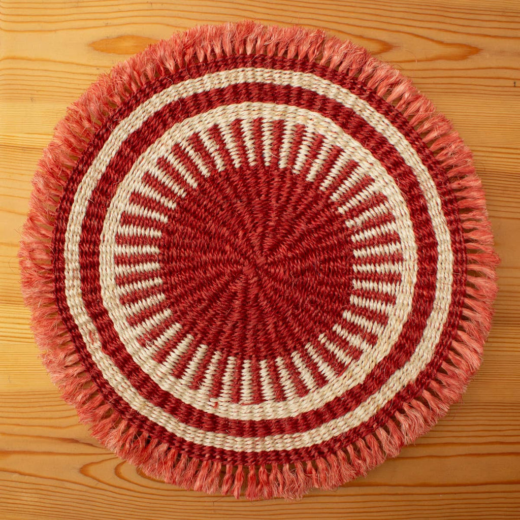 Round woven mat with red and beige pattern on a wooden surface