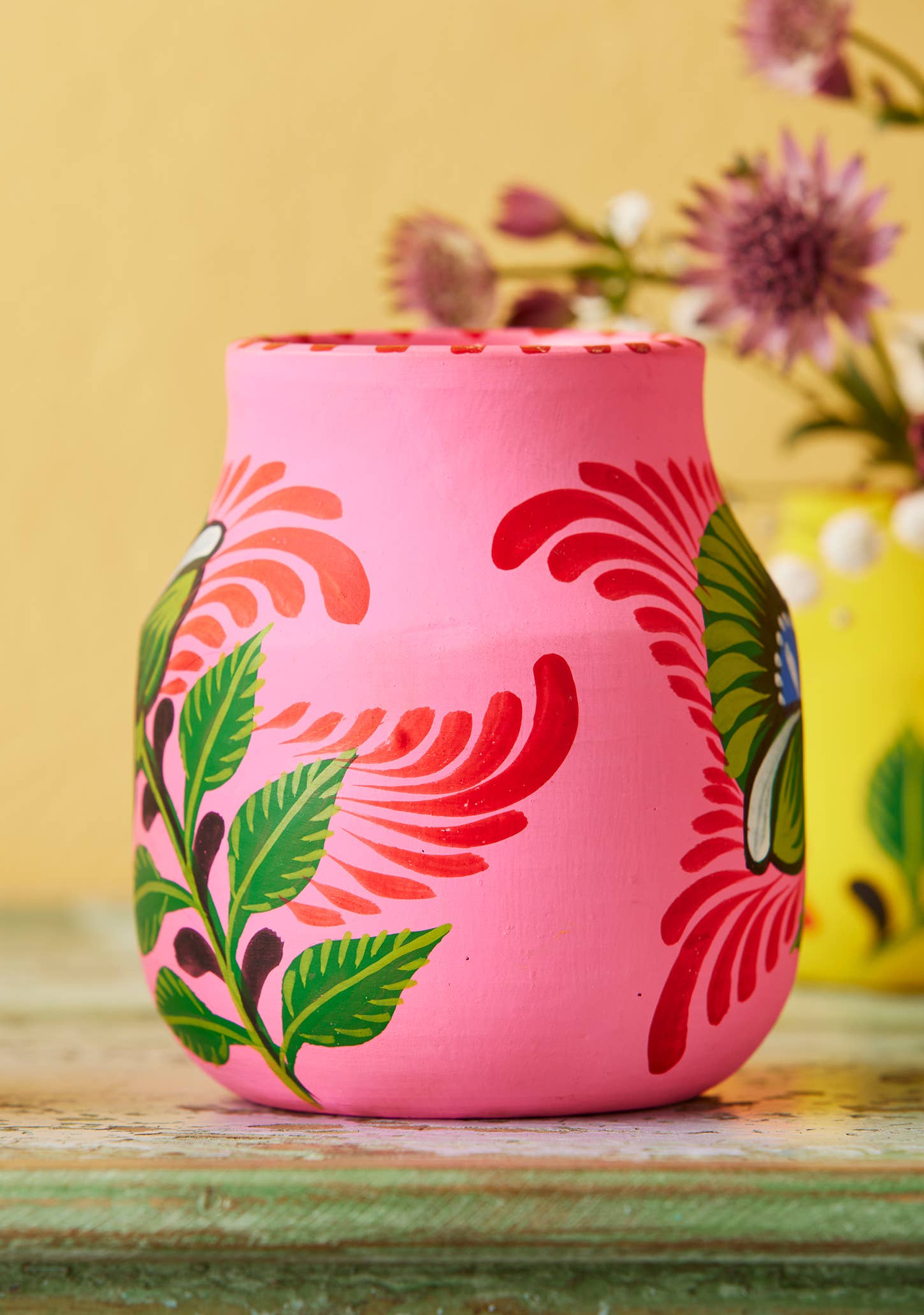 Pink ceramic vase with floral patterns on a wooden surface with a blurred background