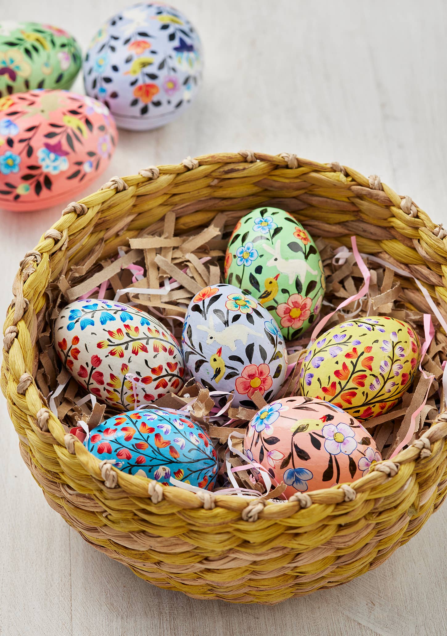 Decorative Easter eggs with floral patterns in a woven basket on a light wooden surface.