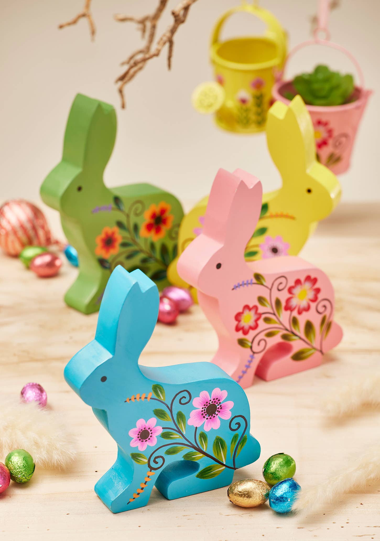 Colorful wooden bunny figurines with floral designs on a wooden surface with Easter eggs.