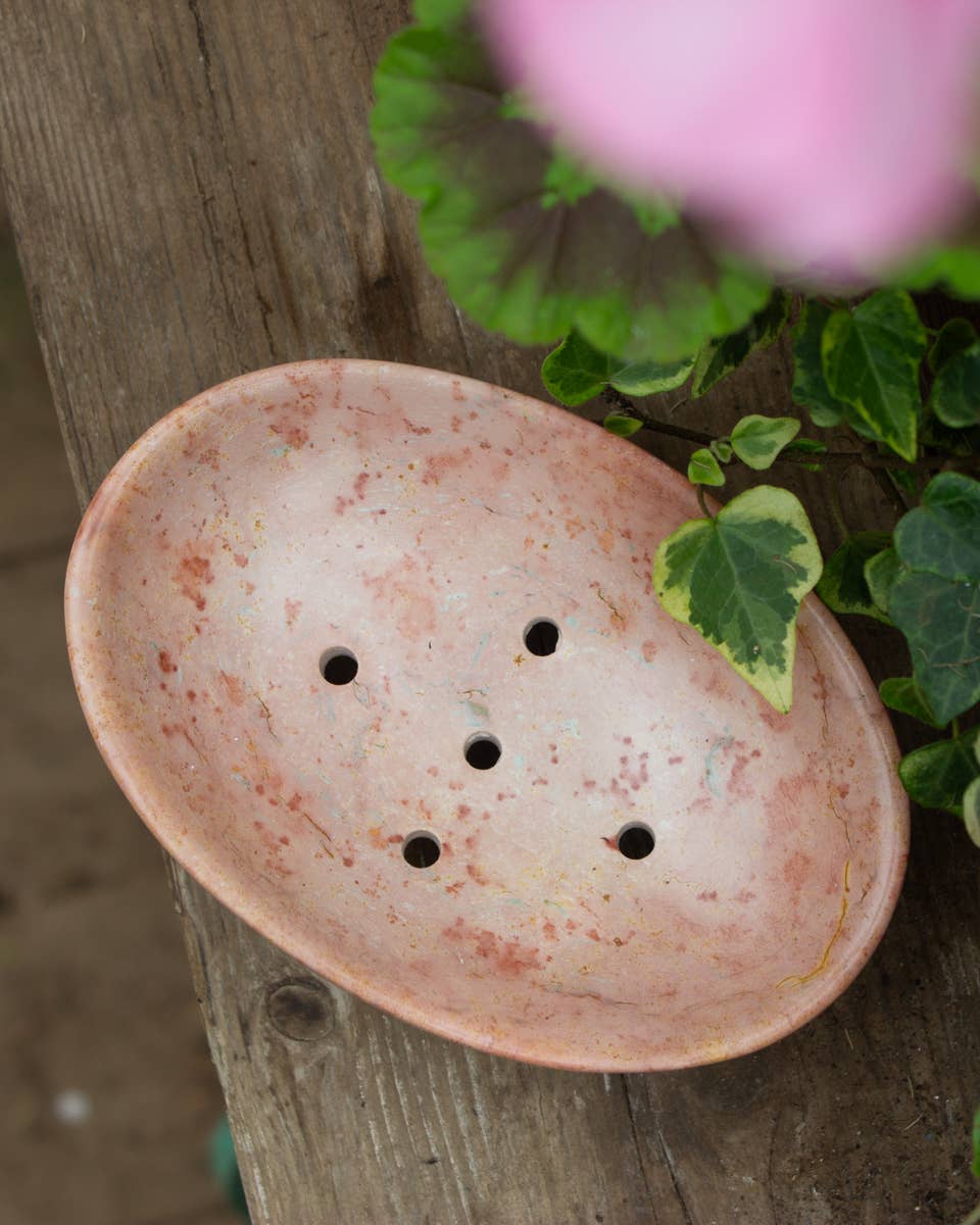 soapstone soap dish with holes on a wooden surface with greenery