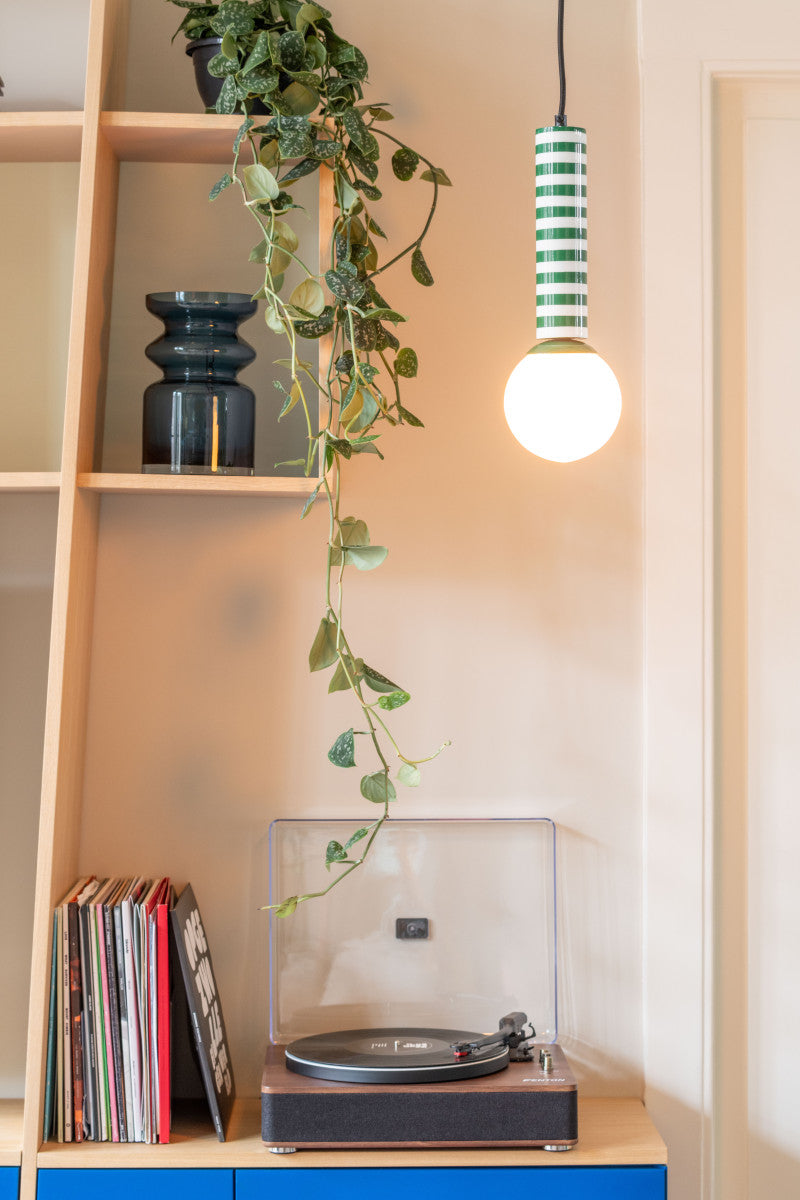 Record player on a shelf with a plant and striped pendant light.