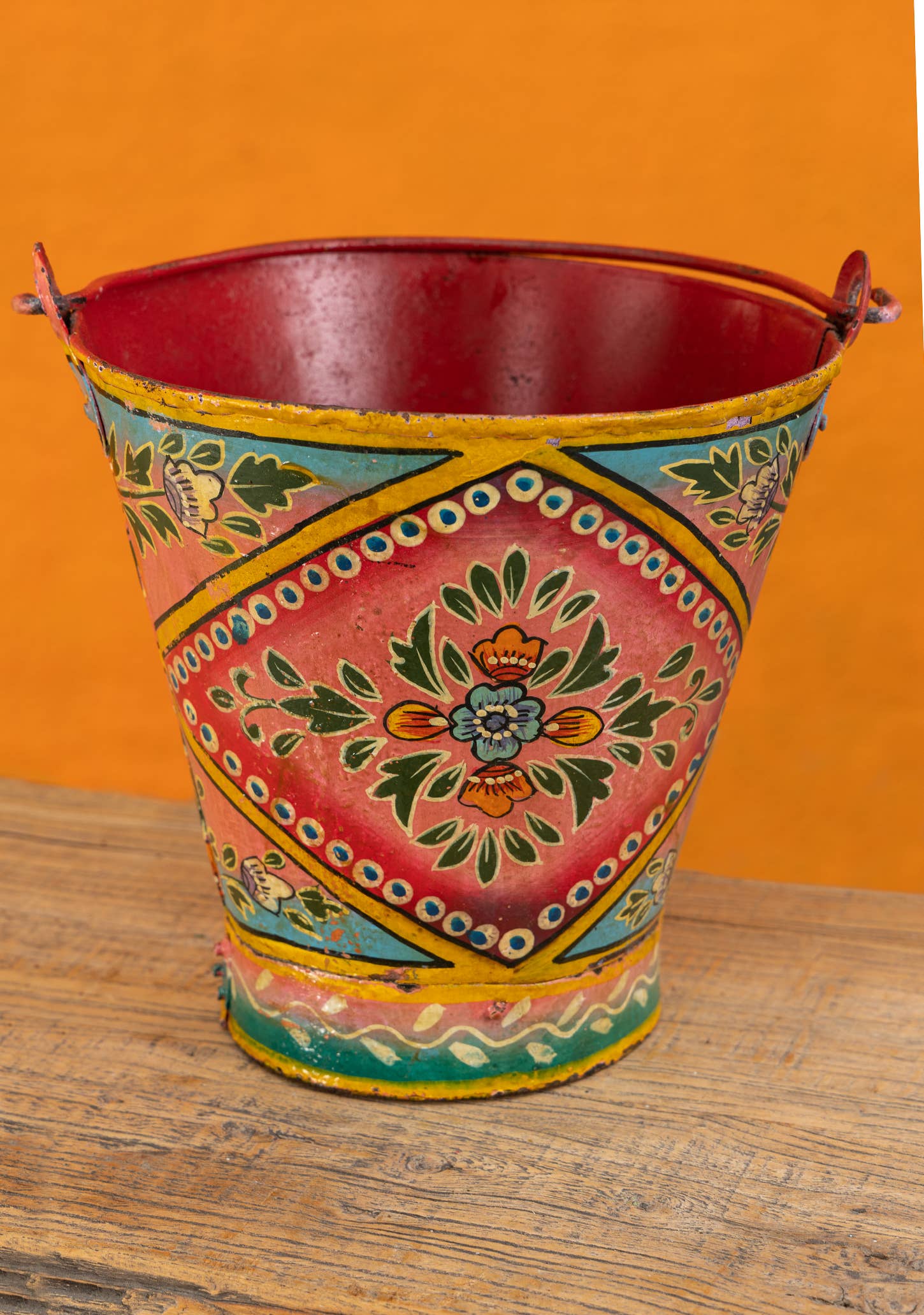 Decorative metal bucket with colorful patterns on a wooden surface and orange background