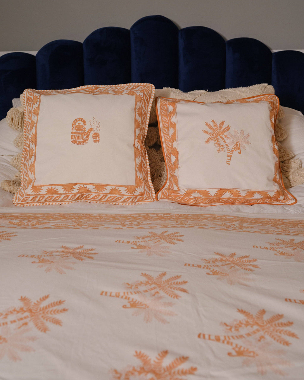 Decorative bedspread with orange floral patterns on a bed with a dark blue headboard.