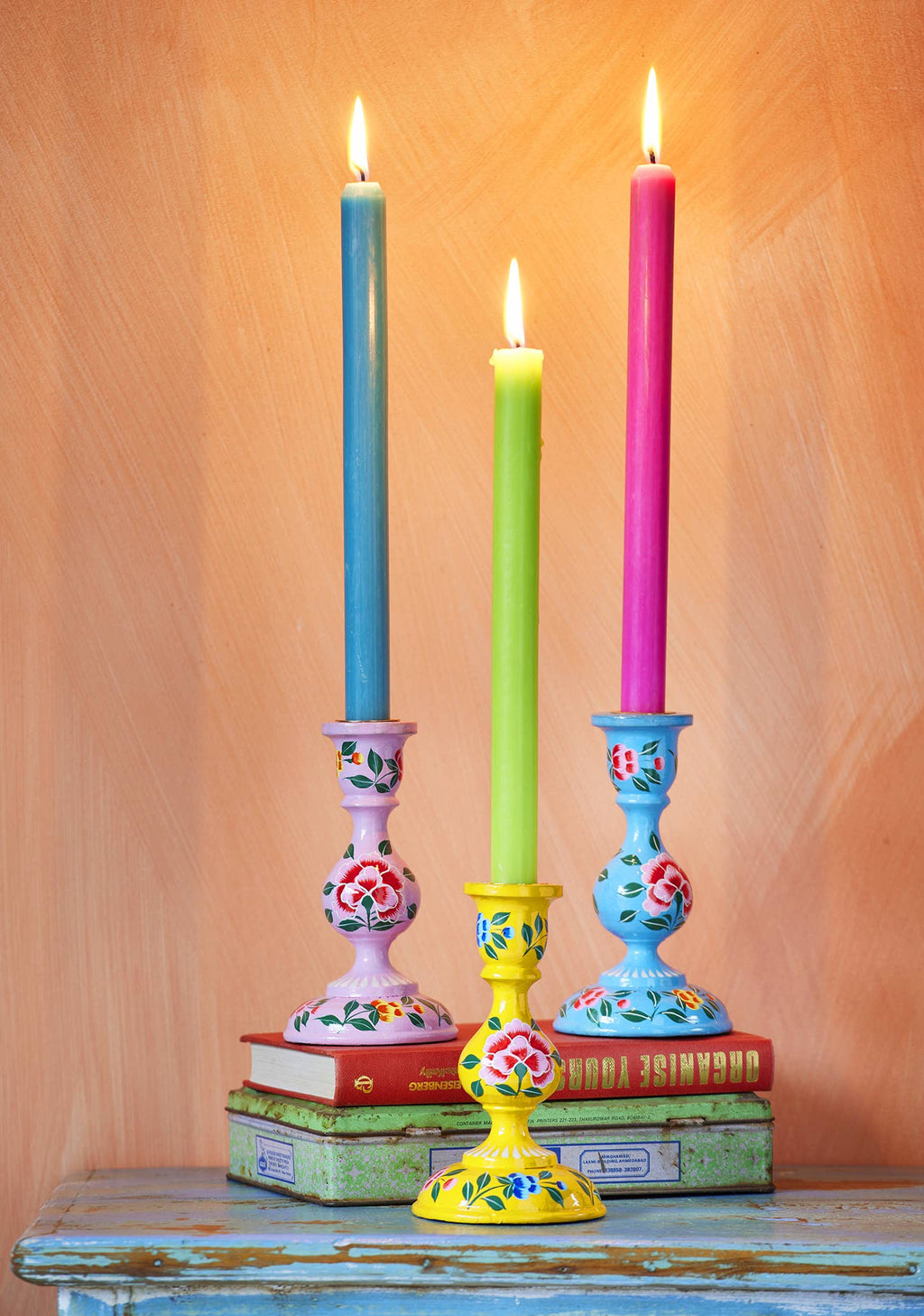 Three colorful candles in decorative candlesticks on a wooden surface.