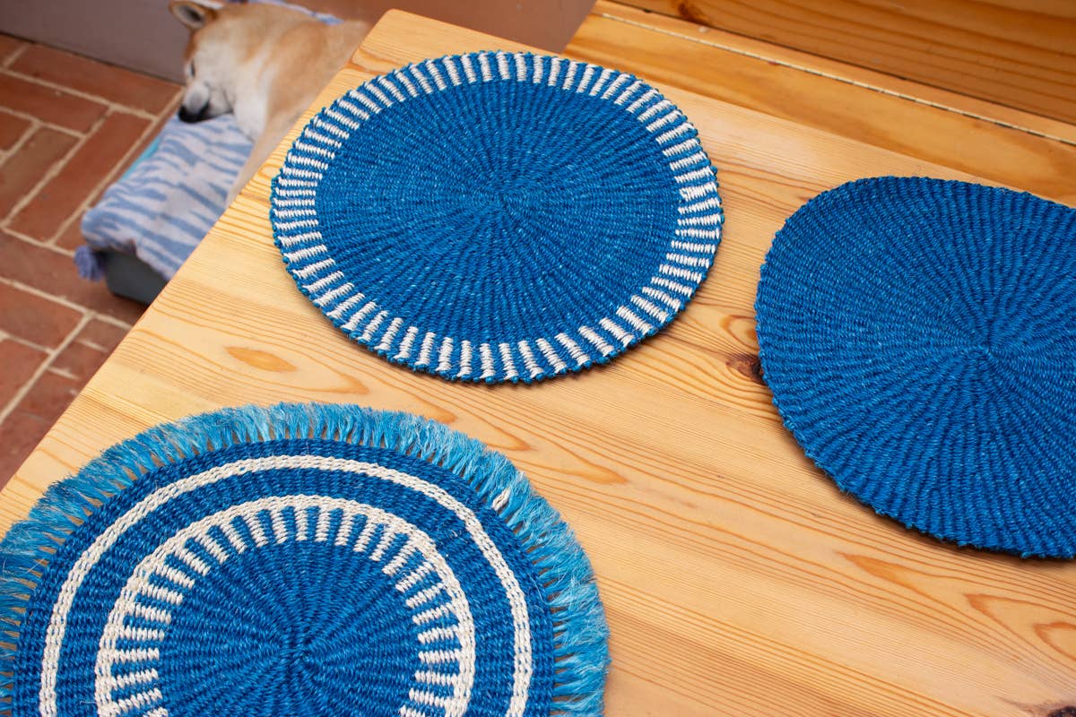Three blue woven placemats with white trim on a wooden table.