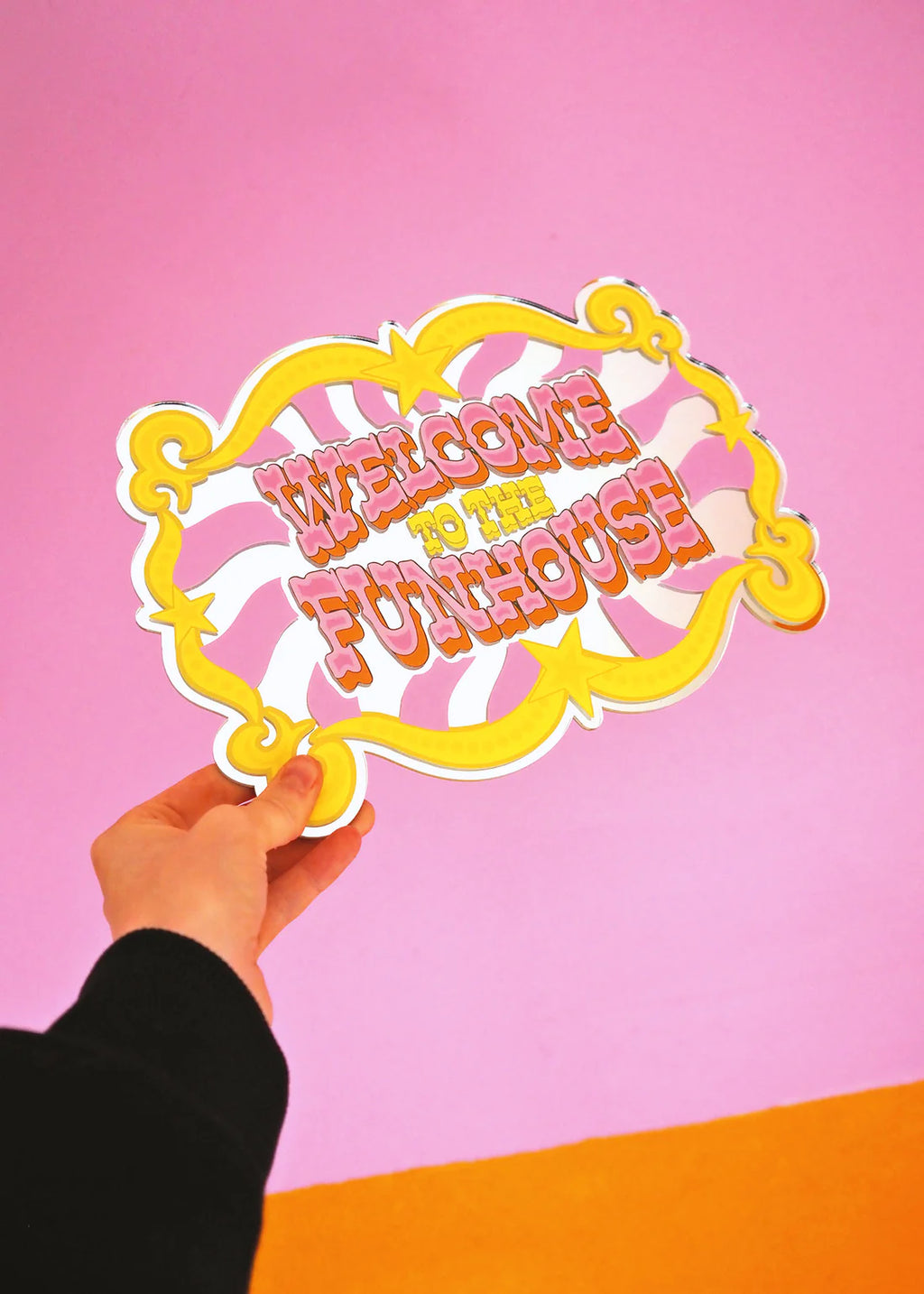 Hand holding a 'Welcome to the Funhouse' sign against a pink and orange gradient background