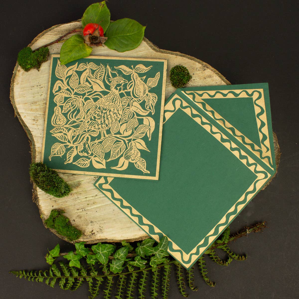 Two green greeting cards with nature-themed designs on a wooden surface with foliage.