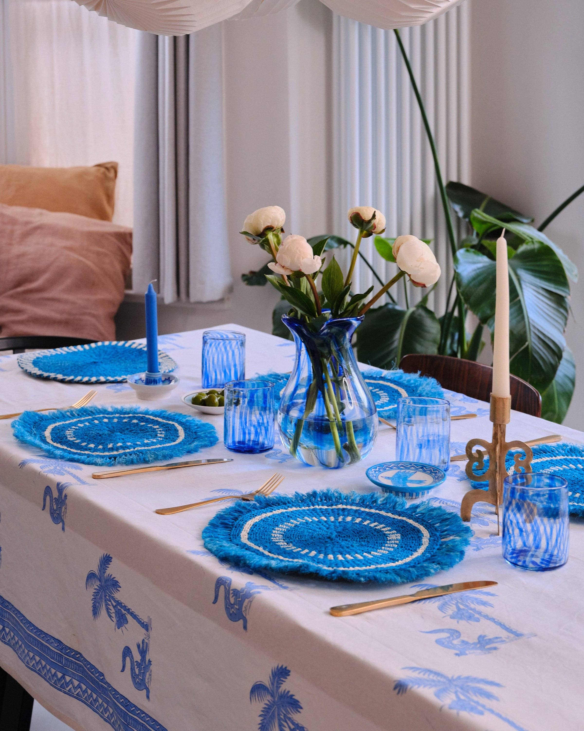 Dining table set with blue and white decor, including plates, glasses, and a vase with flowers.