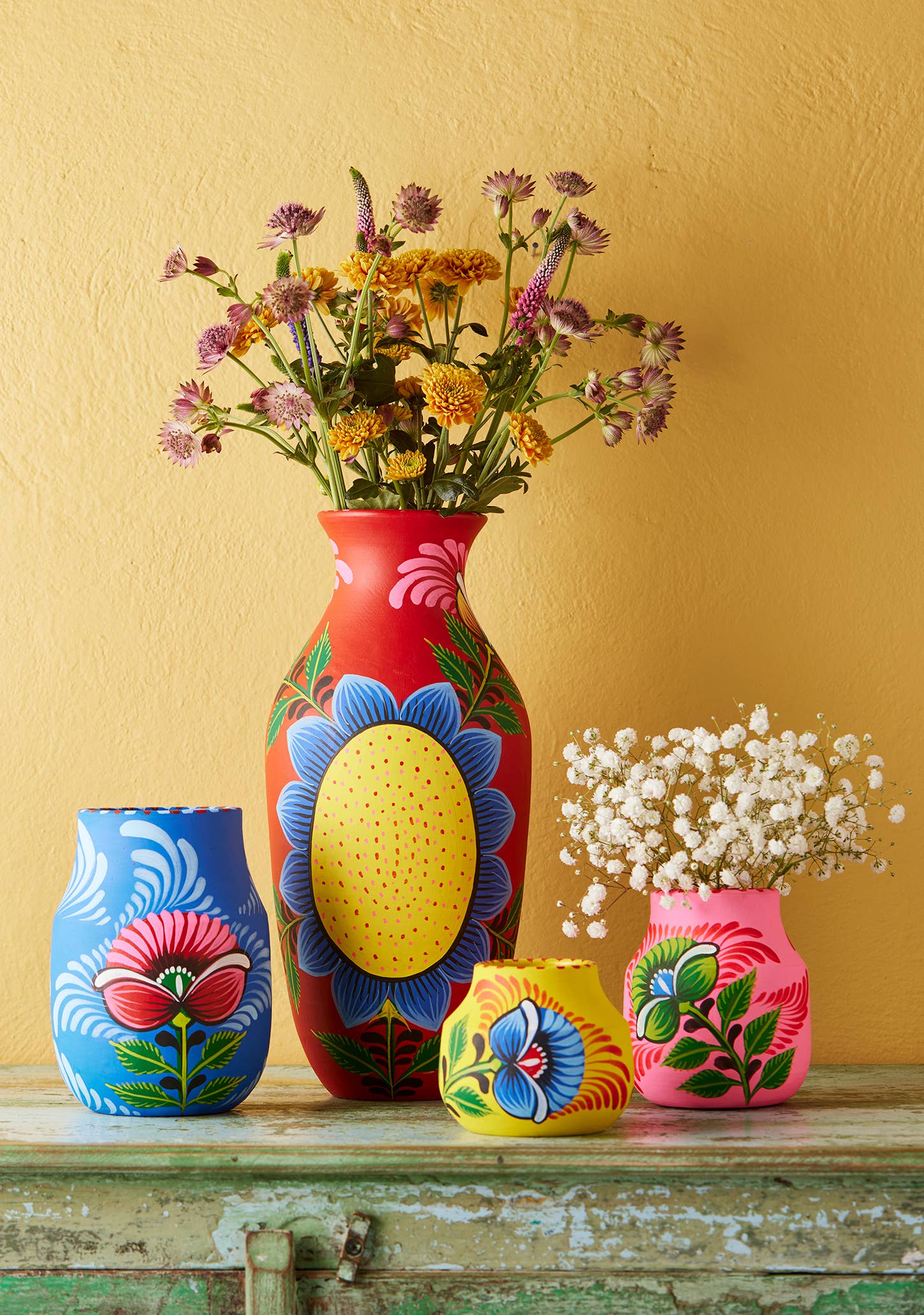 Colorful hand-painted vases with floral designs on a wooden surface against a yellow wall.