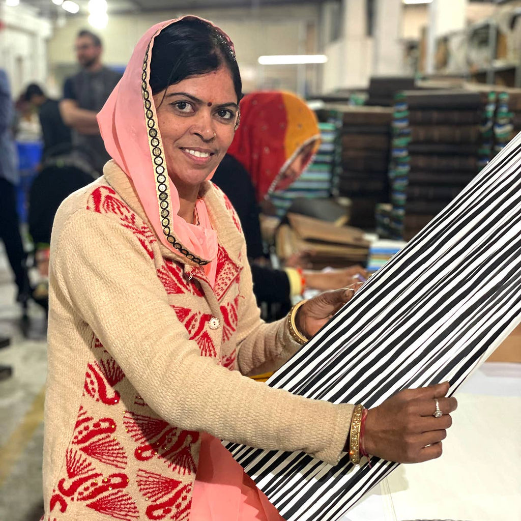 Woman holding fabric in an indoor setting with stacks of boxes in the background