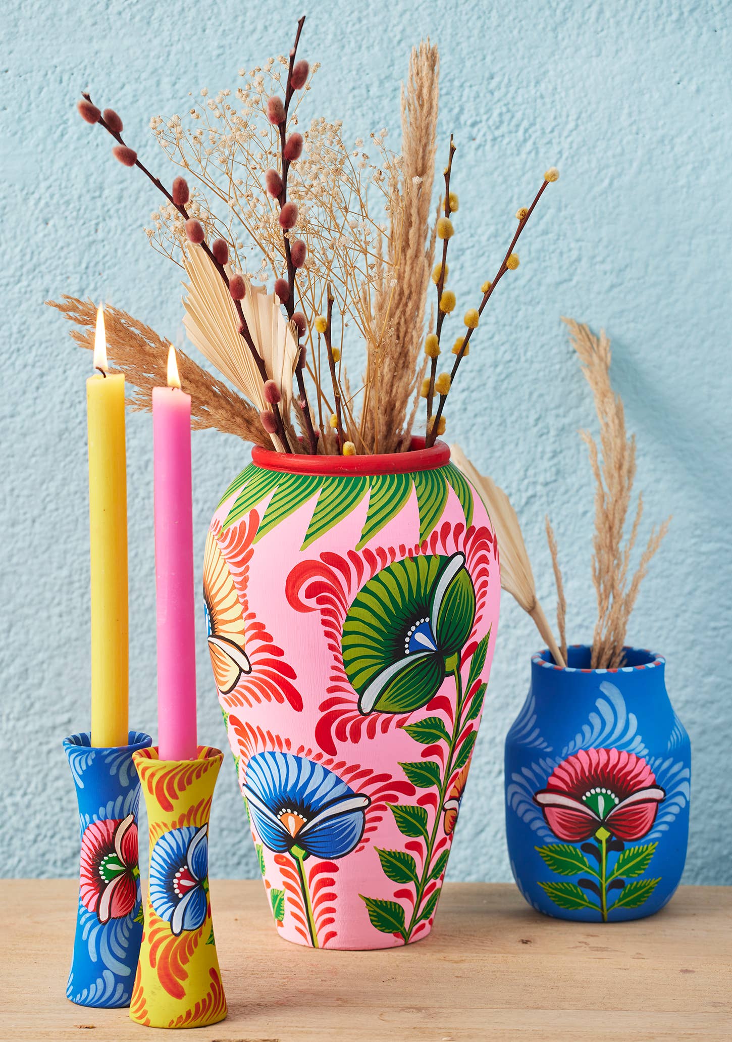 Colorful hand-painted vases with floral patterns on a wooden surface against a light blue wall.