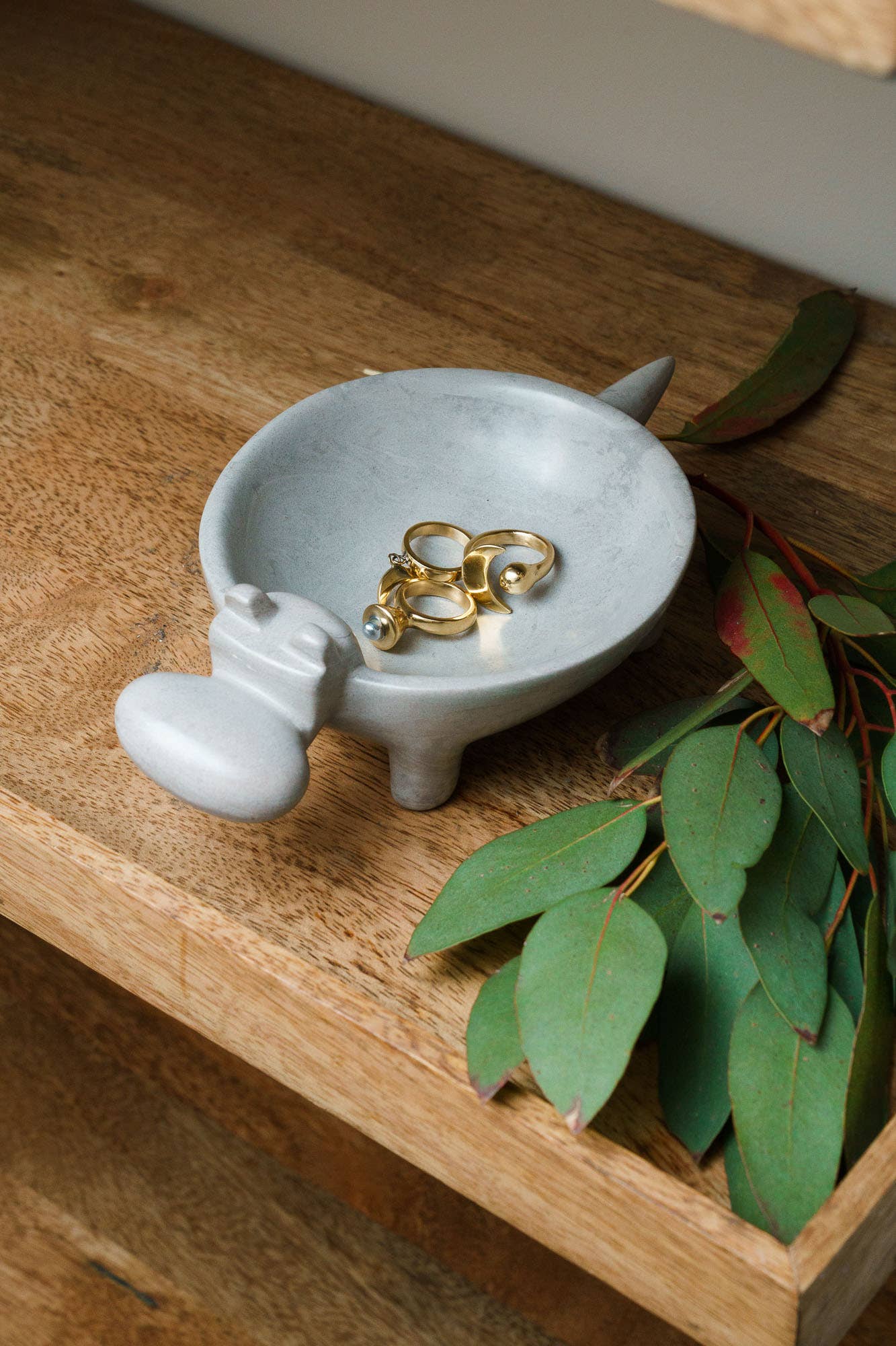 Small soapstone dish with gold rings on a wooden surface with green leaves.