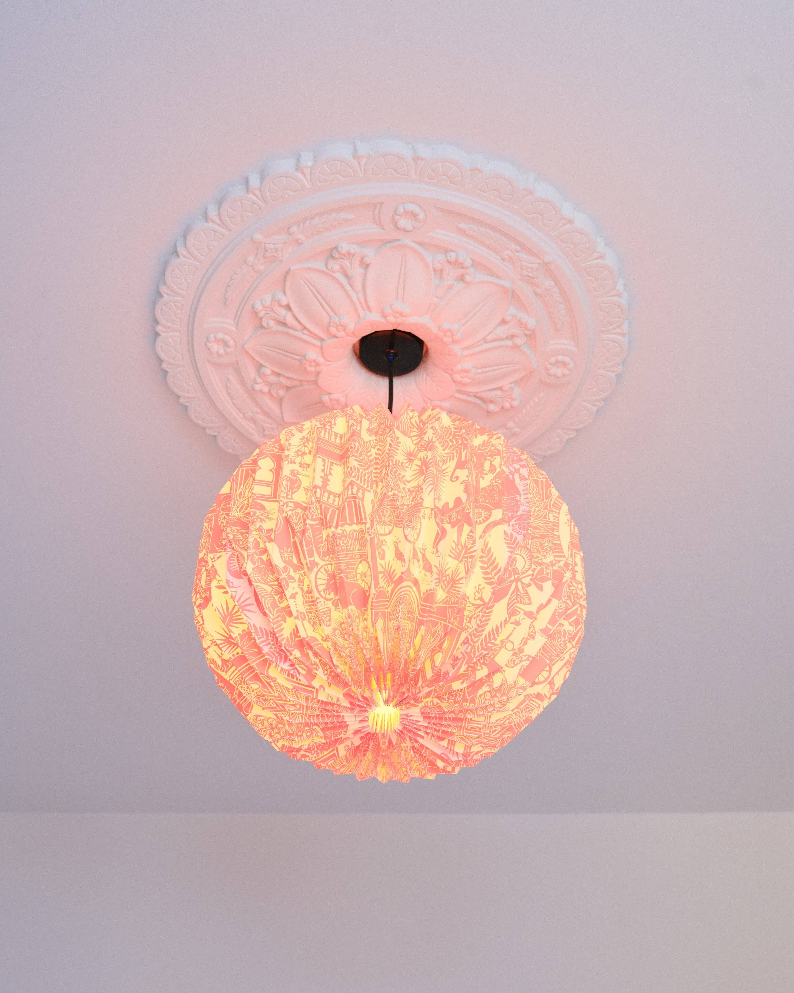 Decorative ceiling light fixture with a pinkish hue on a white ceiling.