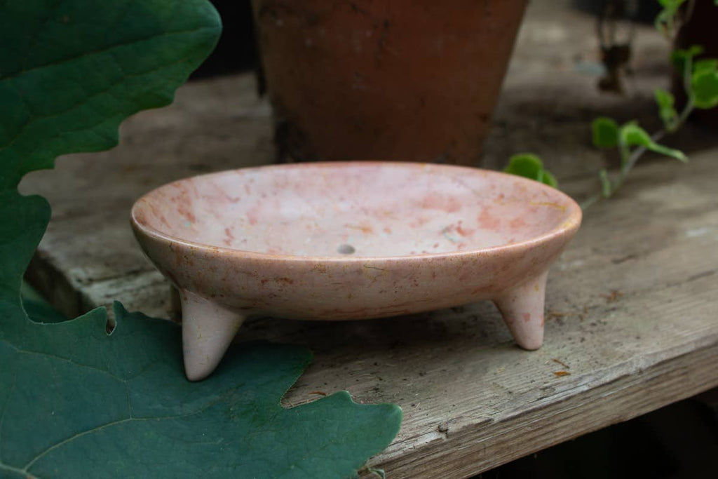 Pink soapstone dish on a wooden surface with a leaf in the foreground