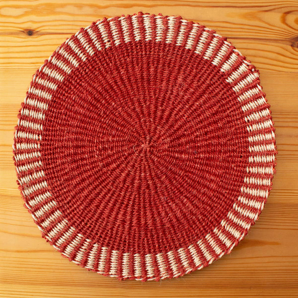 Round woven placemat with red and beige pattern on a wooden surface