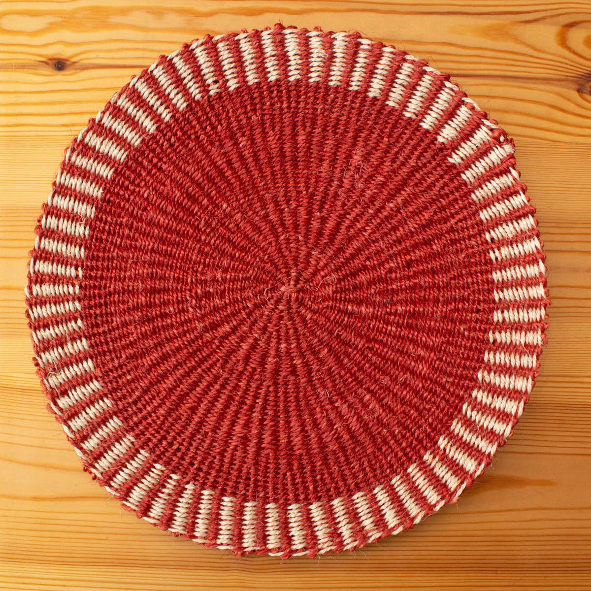 Round woven placemat with red and beige pattern on a wooden surface