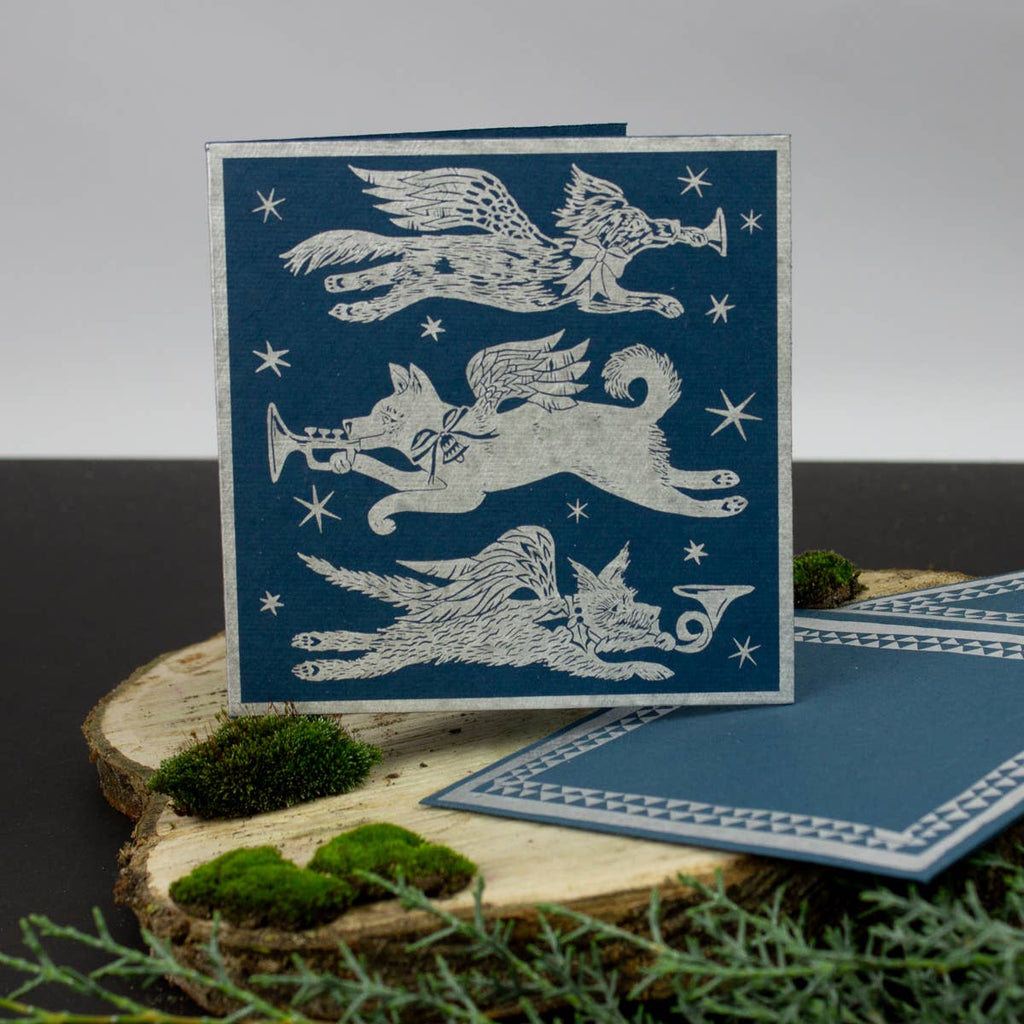 Blue card with white winged creature illustrations on a wooden surface with greenery.