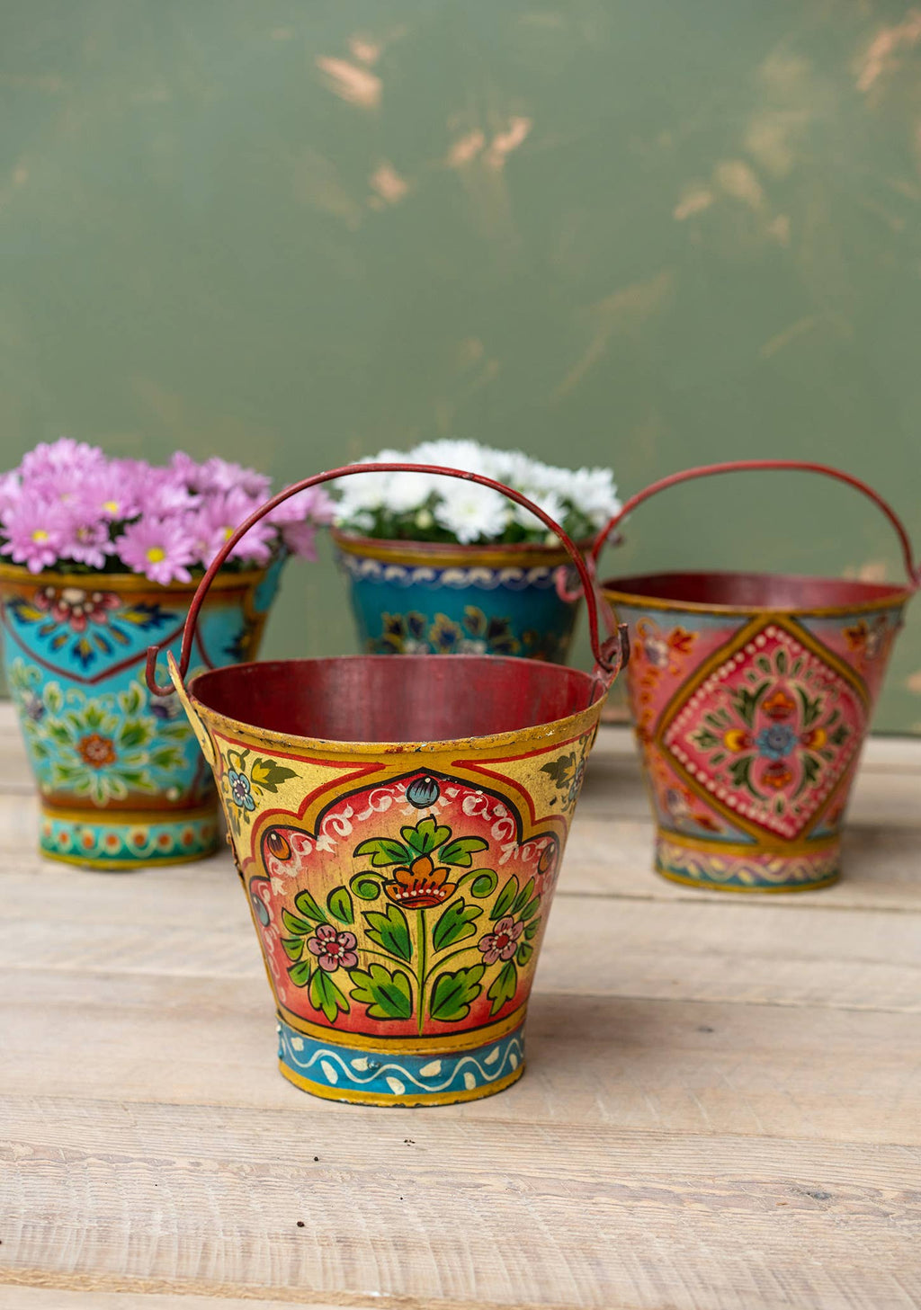 Colorful hand-painted metal buckets with floral designs on a wooden surface.