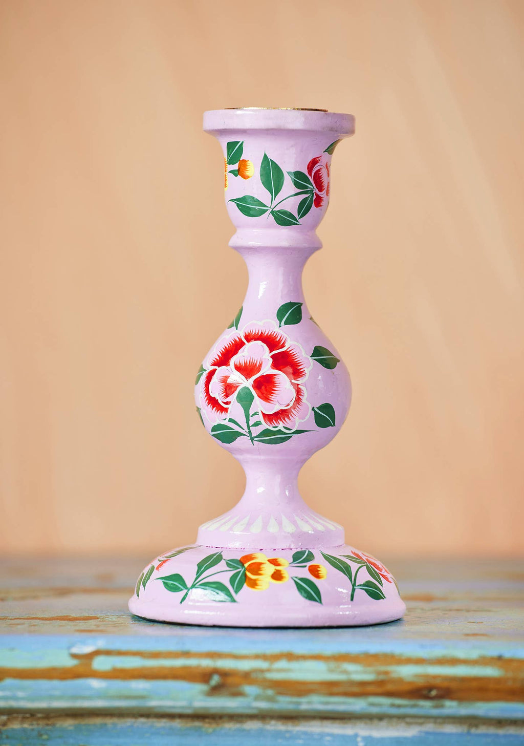 Decorative candle holder with floral designs on a wooden surface and beige background