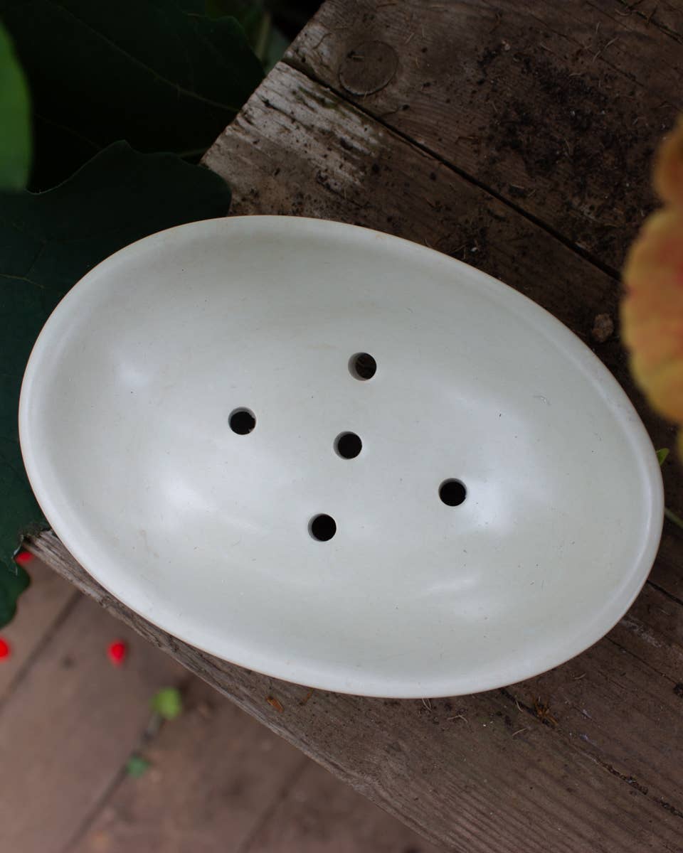 White soapstone soap dish with holes on a wooden surface