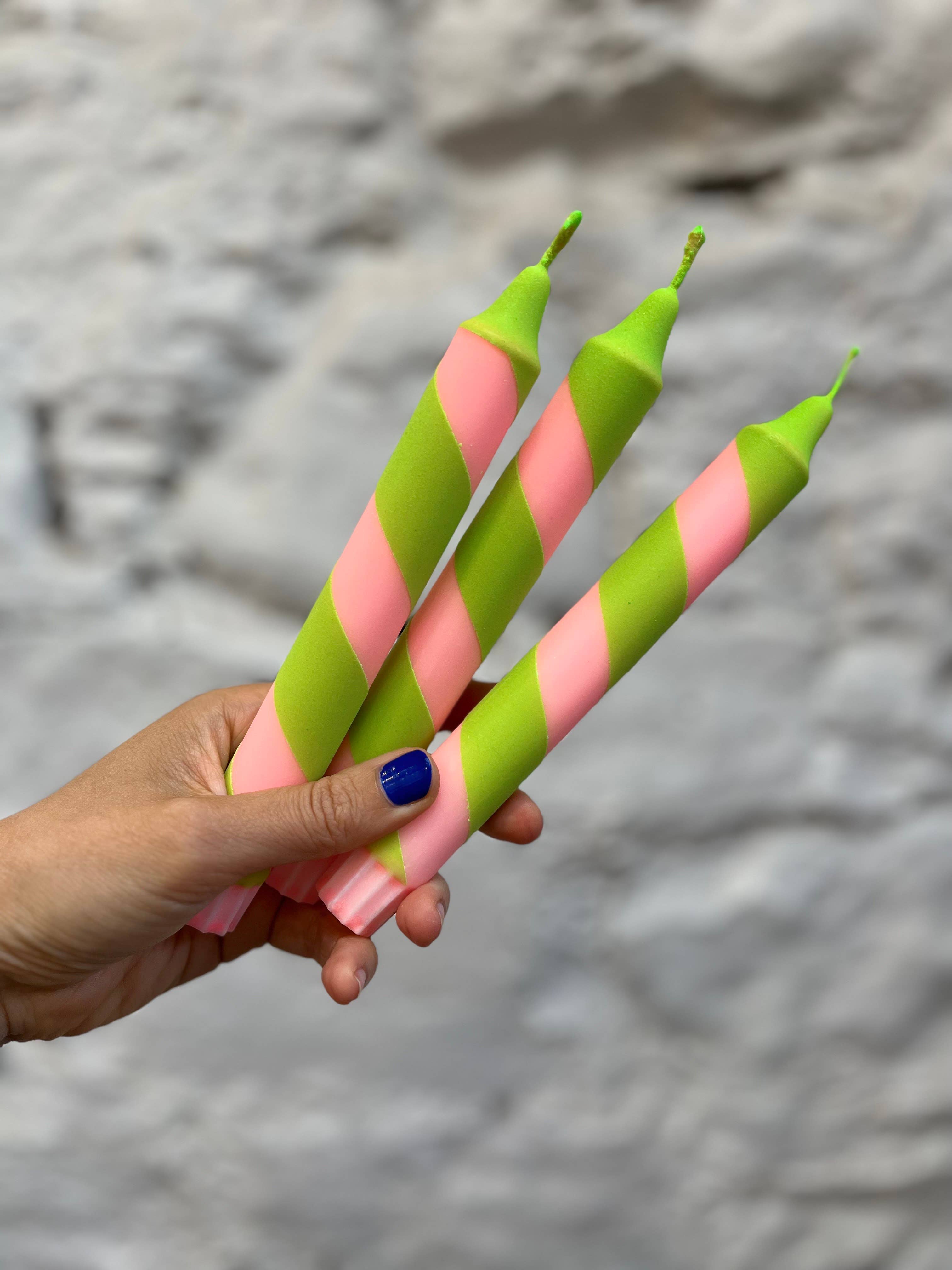 Hand holding two pink and green striped candles against a stone background