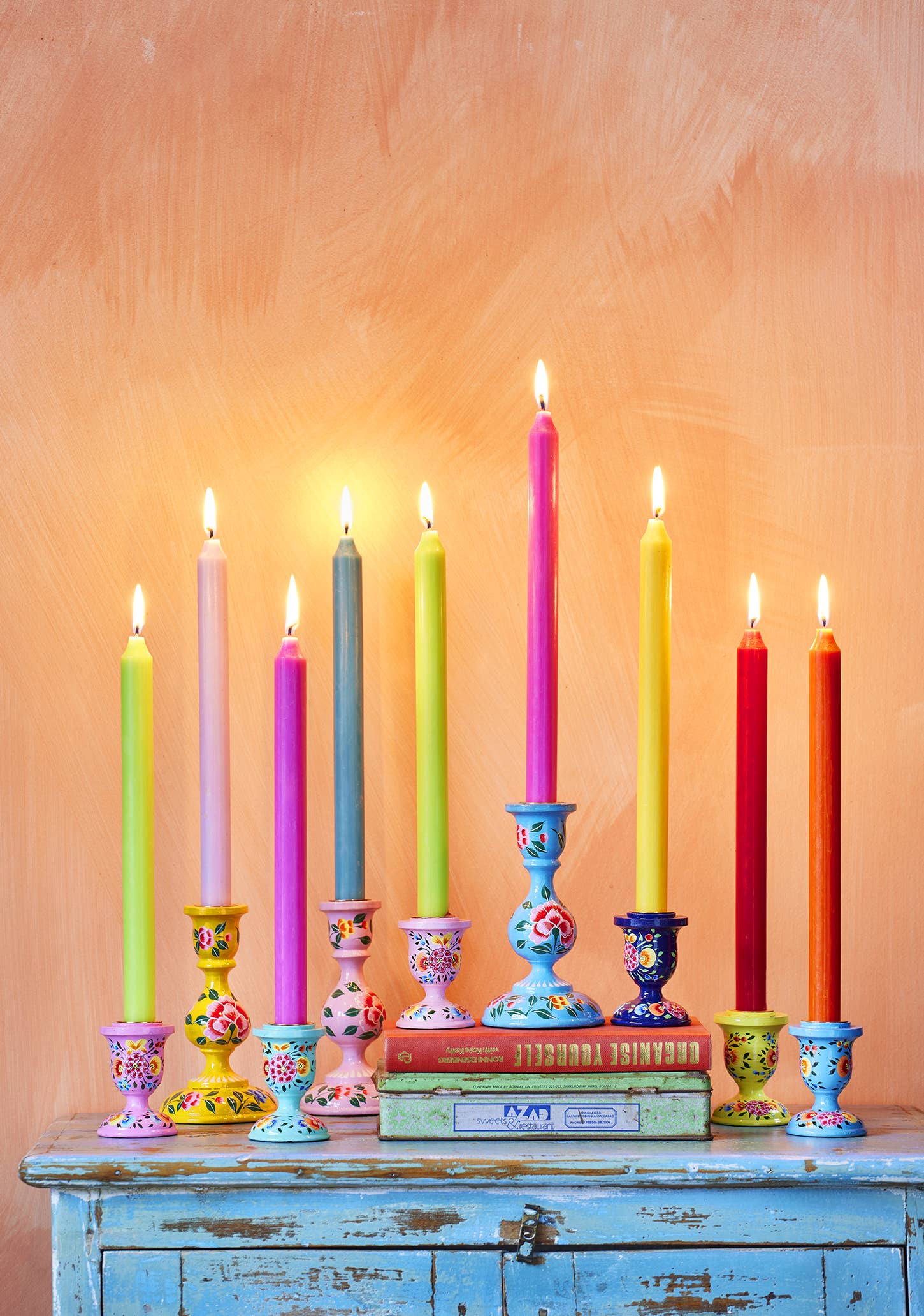 Colorful candles in various holders on a wooden surface with a pastel background