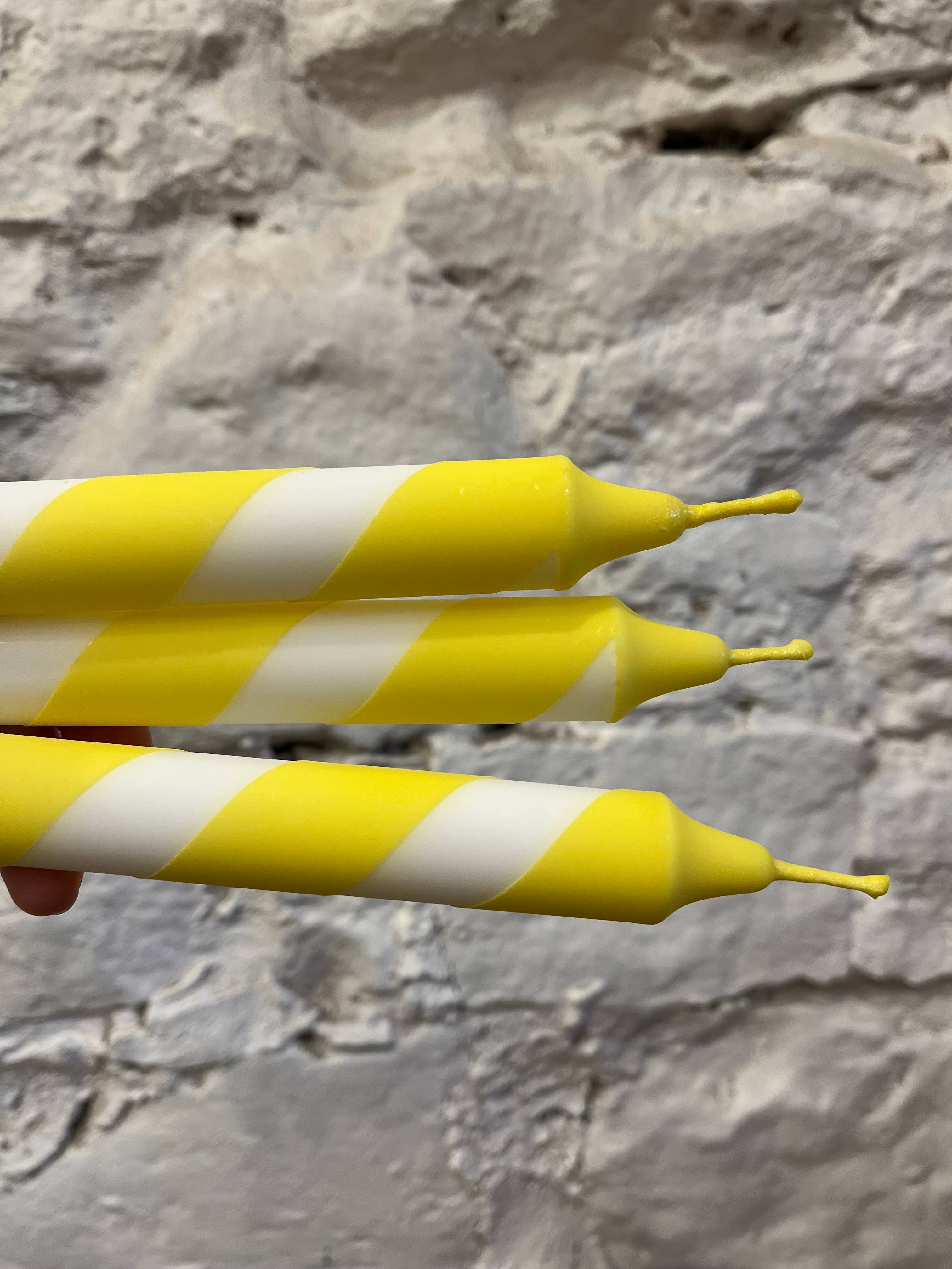 yellow and white striped candles held against a stone wall background