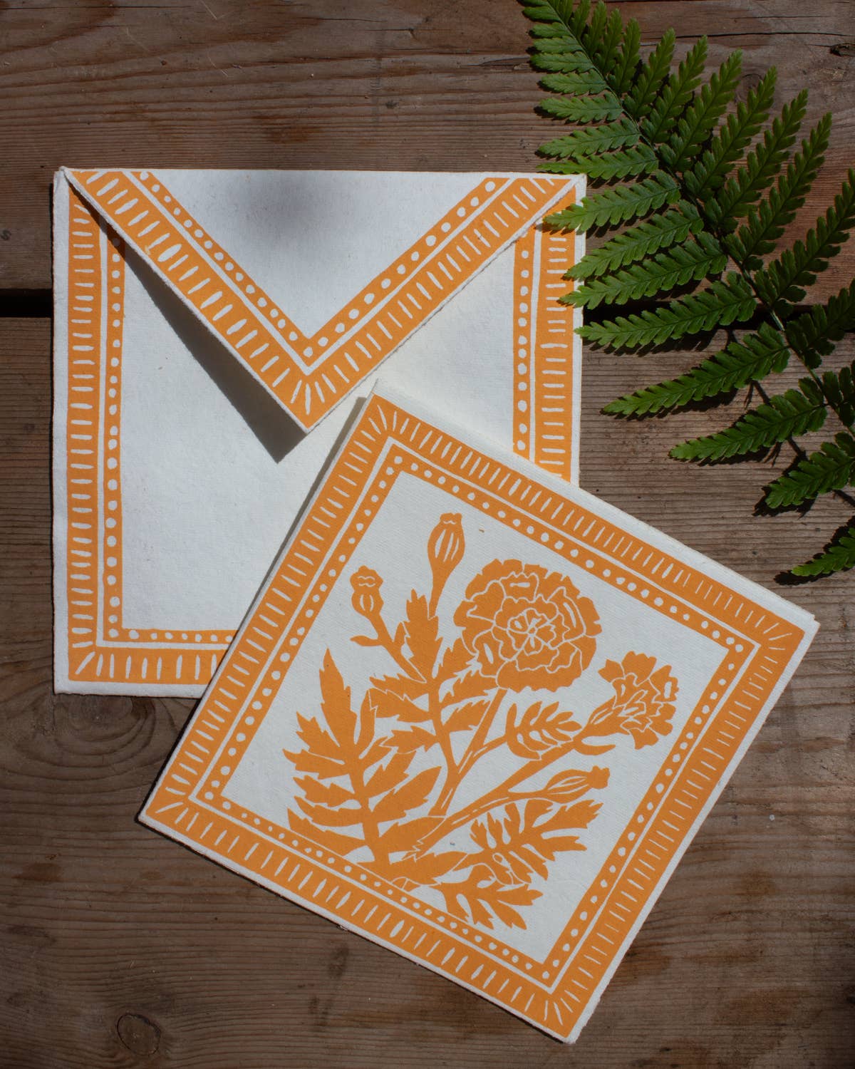 Two white cards with orange borders and floral design on a wooden surface with green leaves.