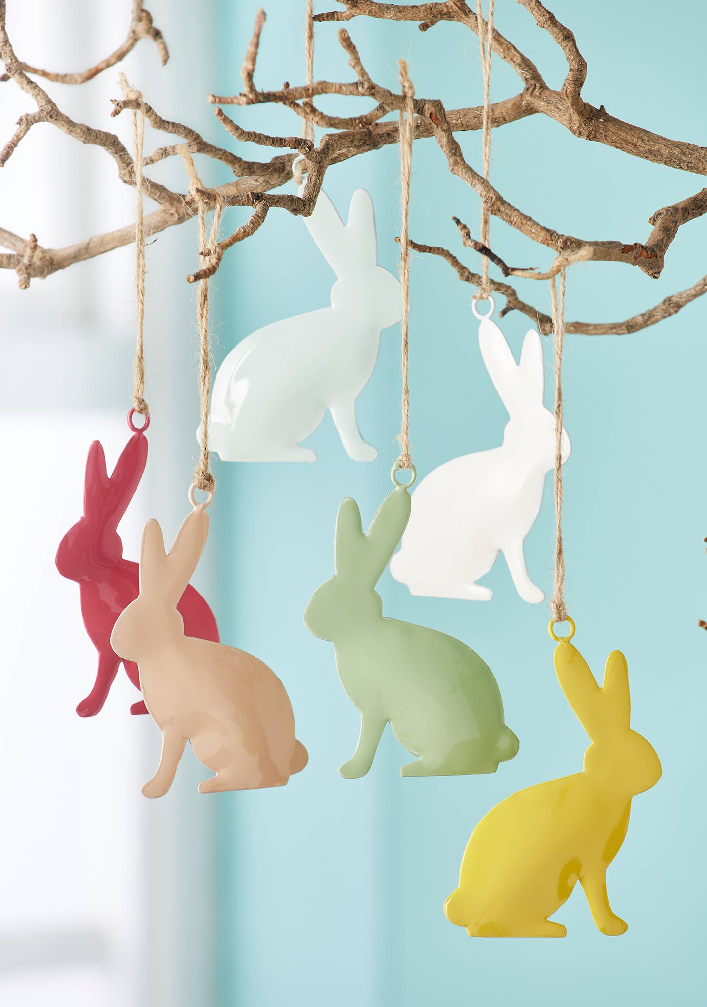 Colorful rabbit-shaped ornaments hanging from a branch against a light blue background