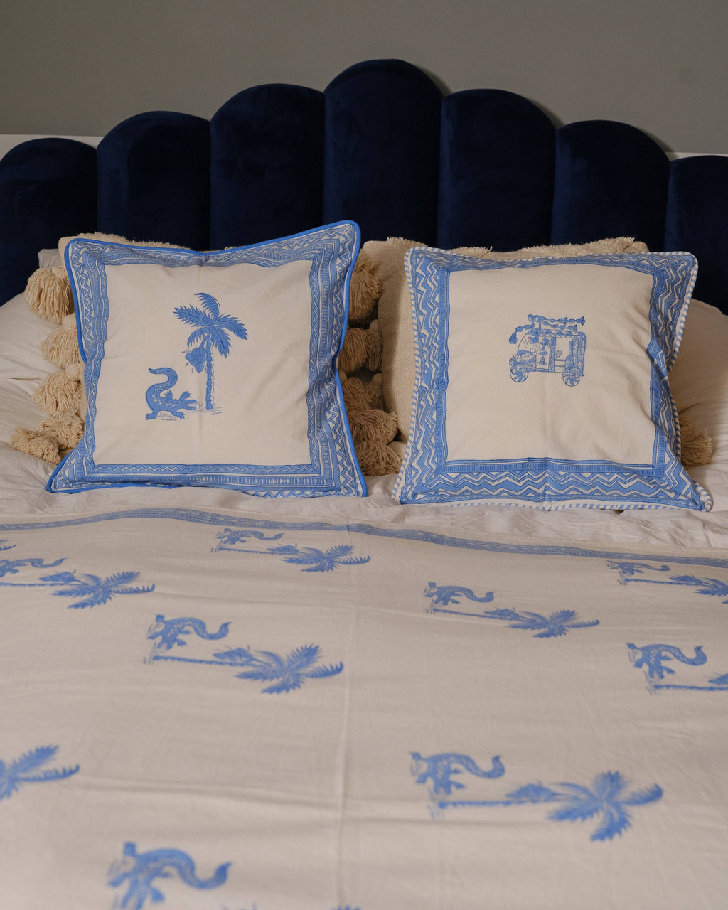 Decorative pillows with blue palm tree designs on a bedspread with similar patterns.