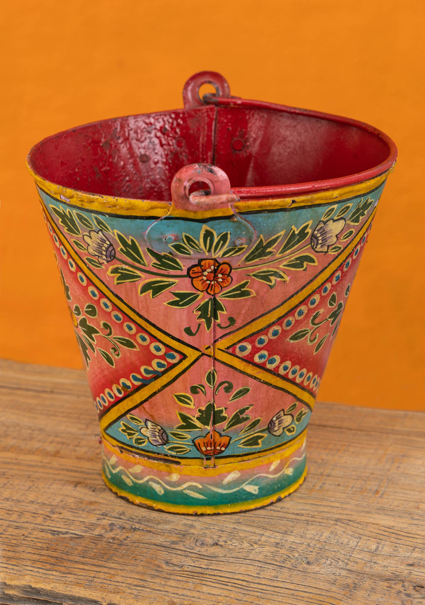 Decorative metal bucket with colorful hand-painted design on a wooden surface.