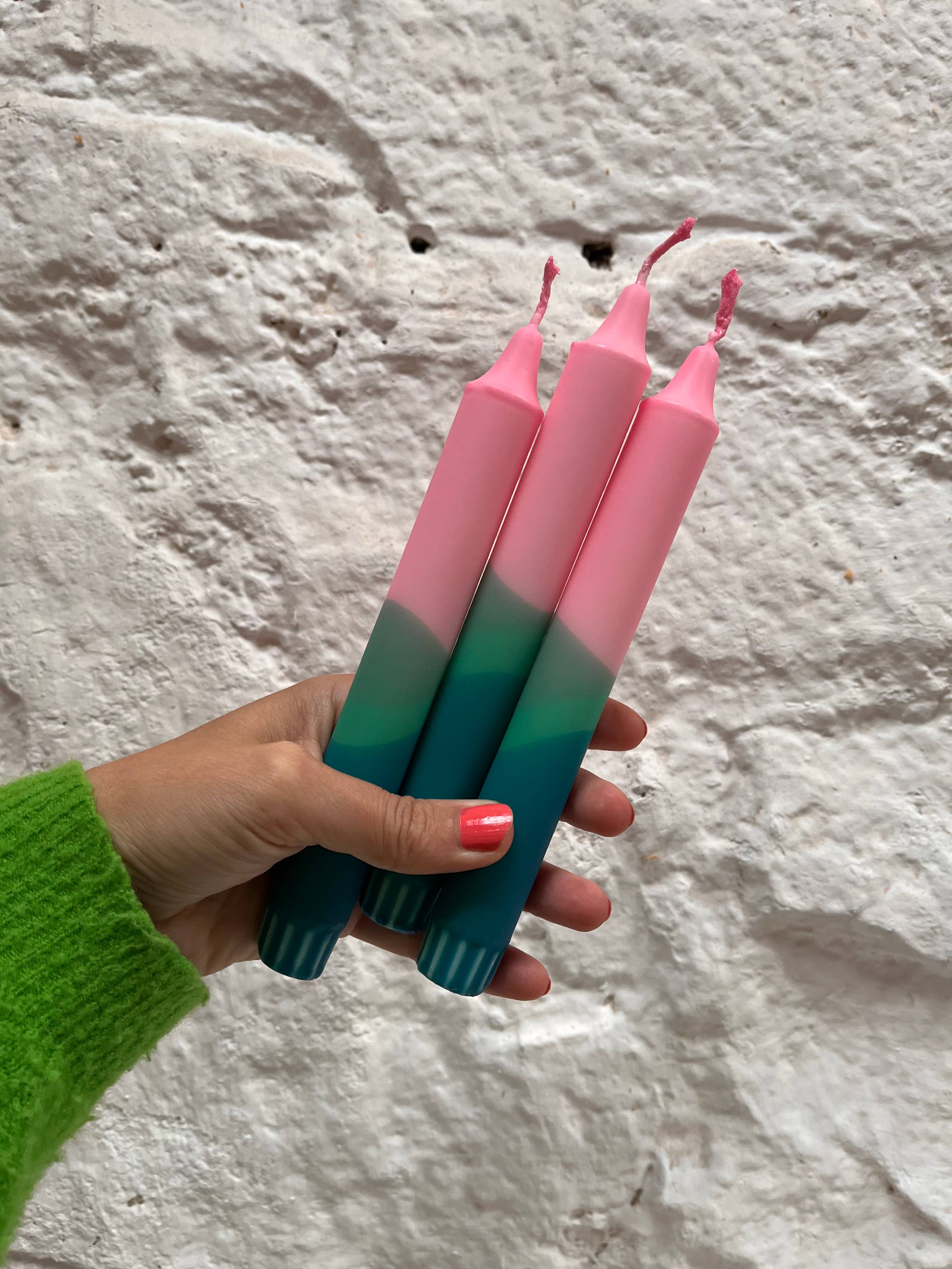 Hand holding three gradient candles against a textured stone wall.