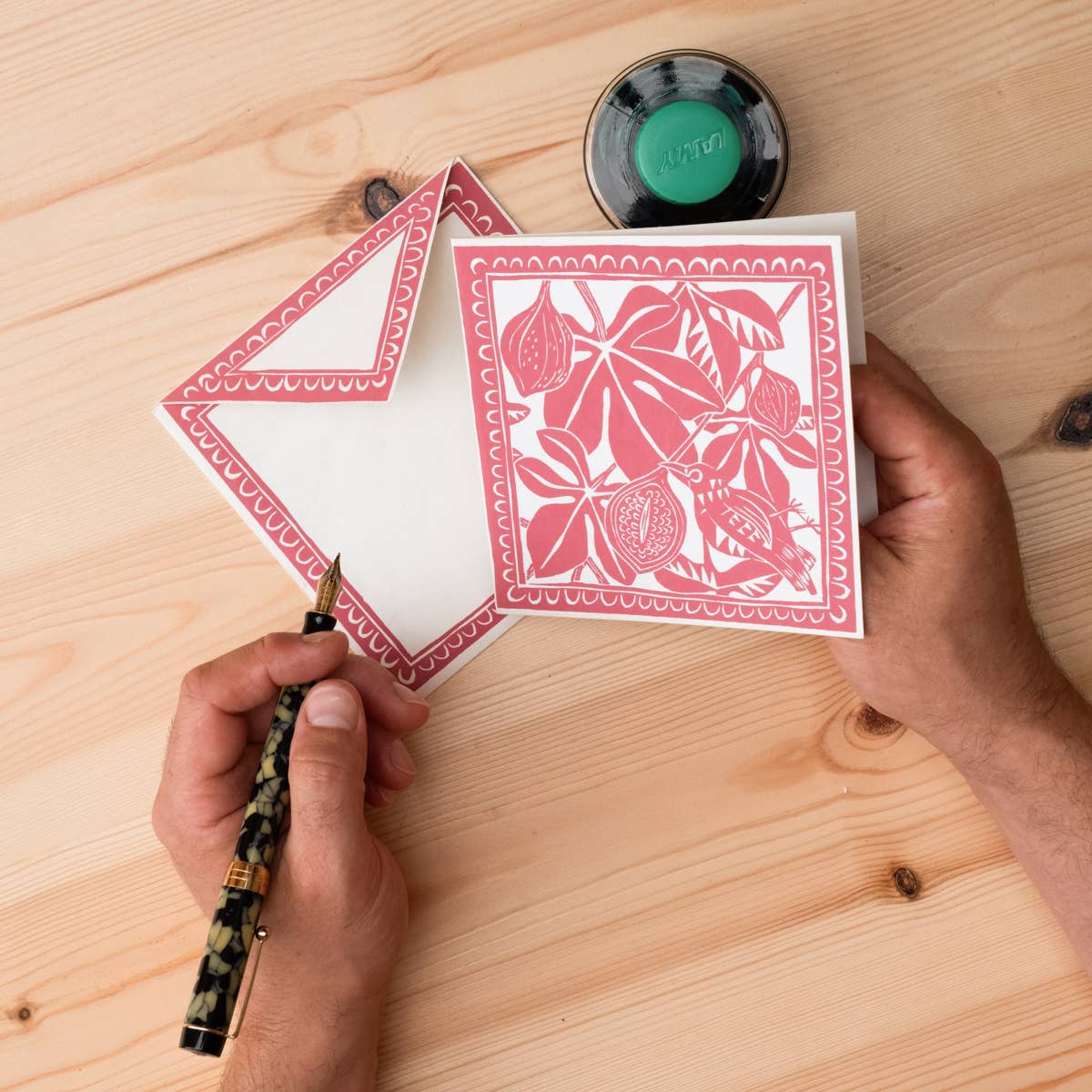 Hand holding a pen with a decorated card on a wooden surface