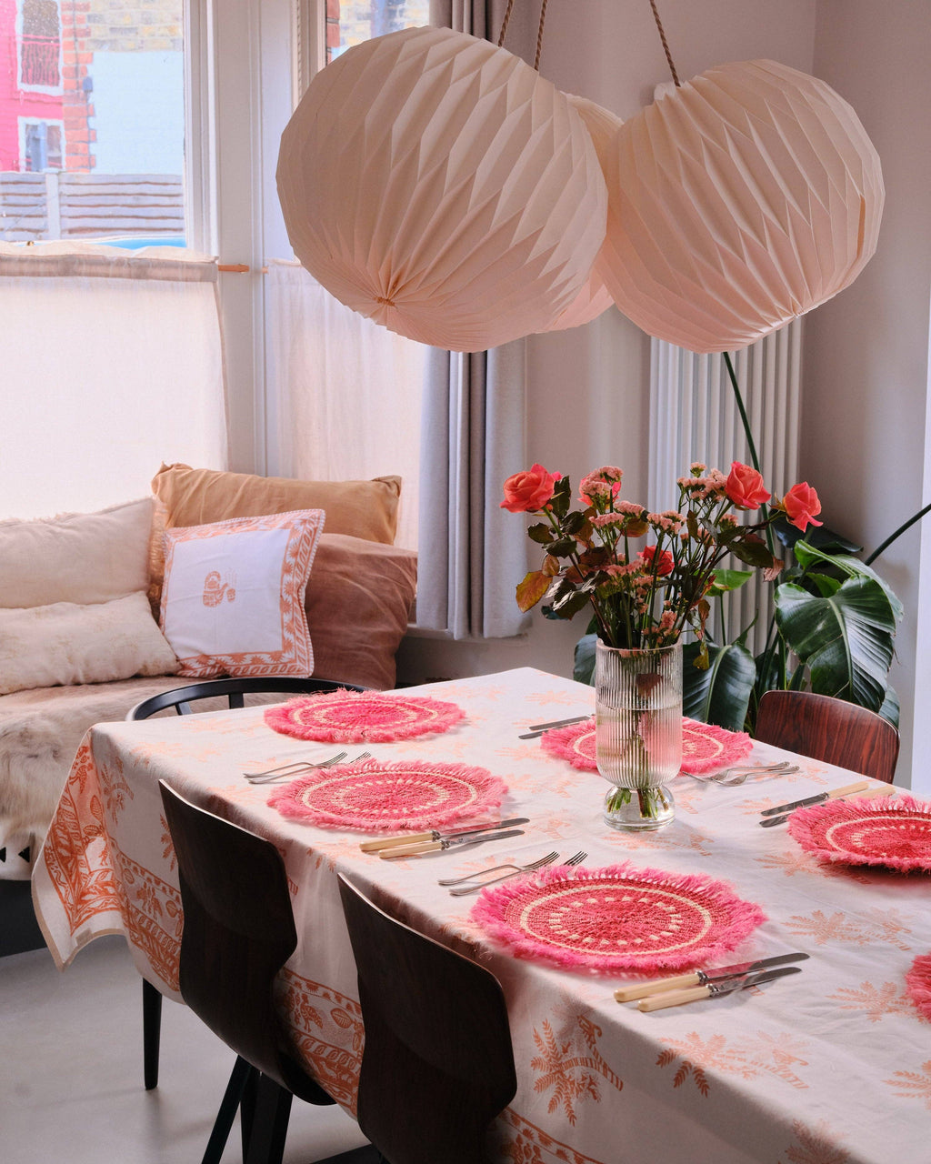Dining table set with pink placemats and a vase of flowers in a living room.
