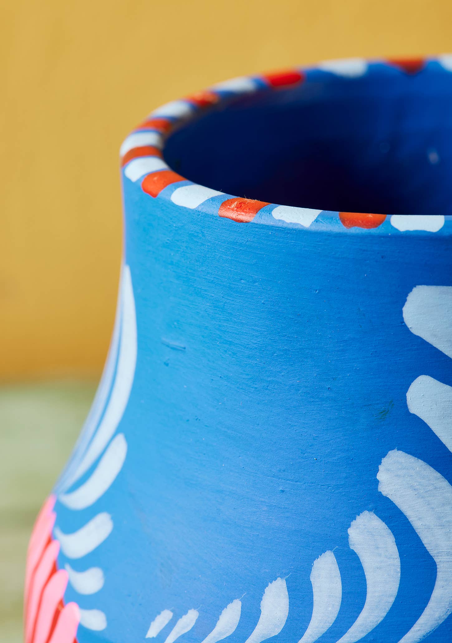 Blue ceramic pot with white, red, and pink patterns on a yellow background