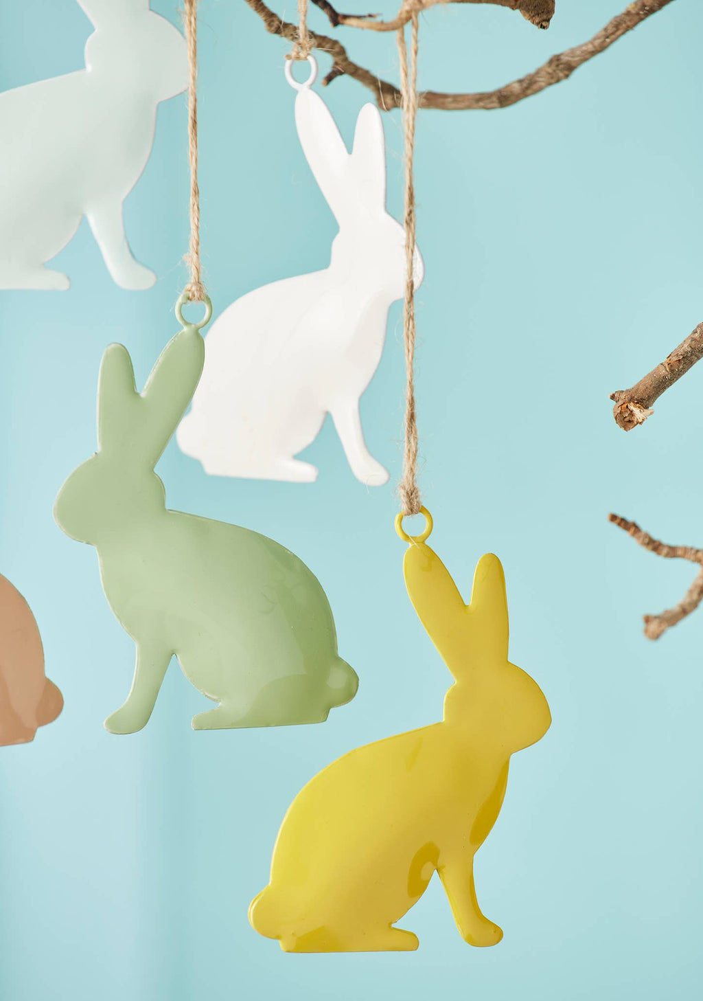 Colorful bunny-shaped ornaments hanging from a branch against a light blue background