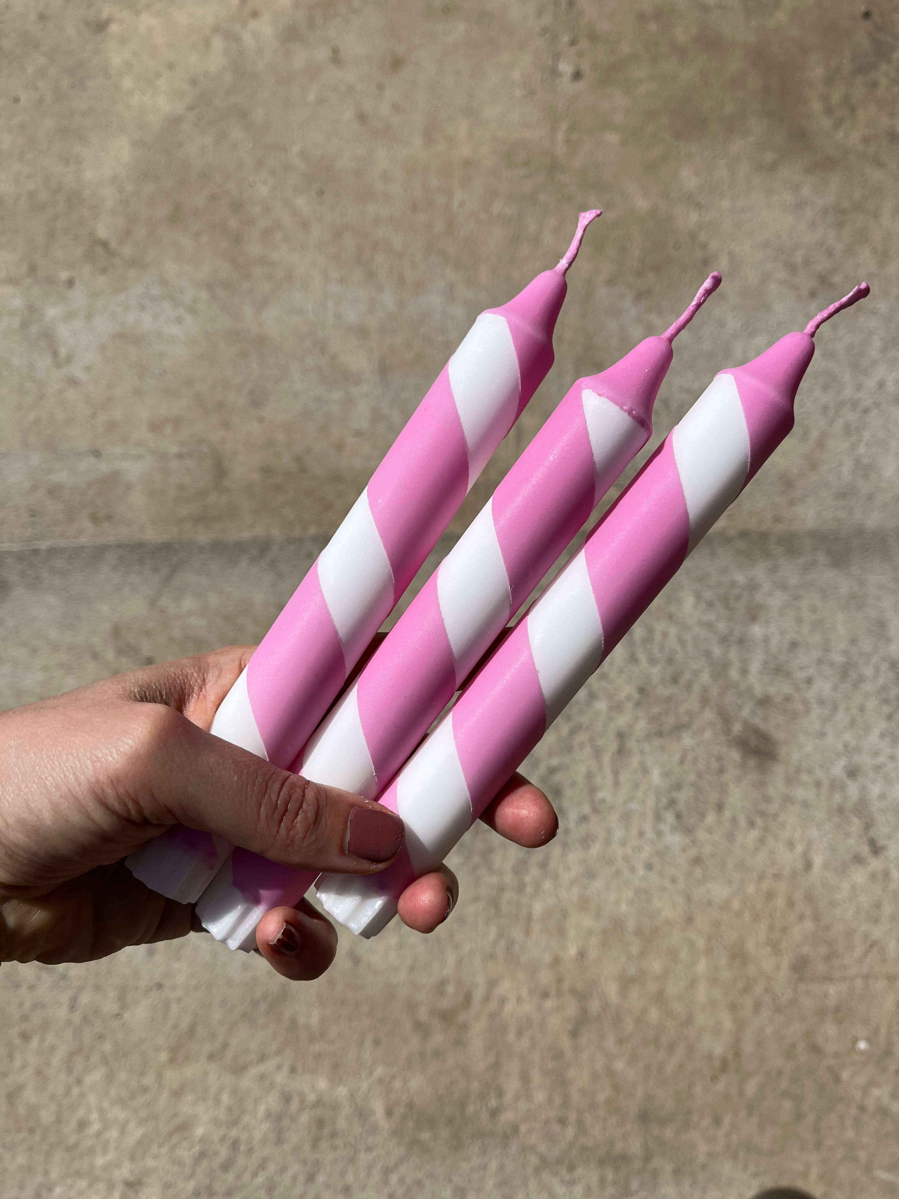 Hand holding three pink and white striped candles against a concrete background