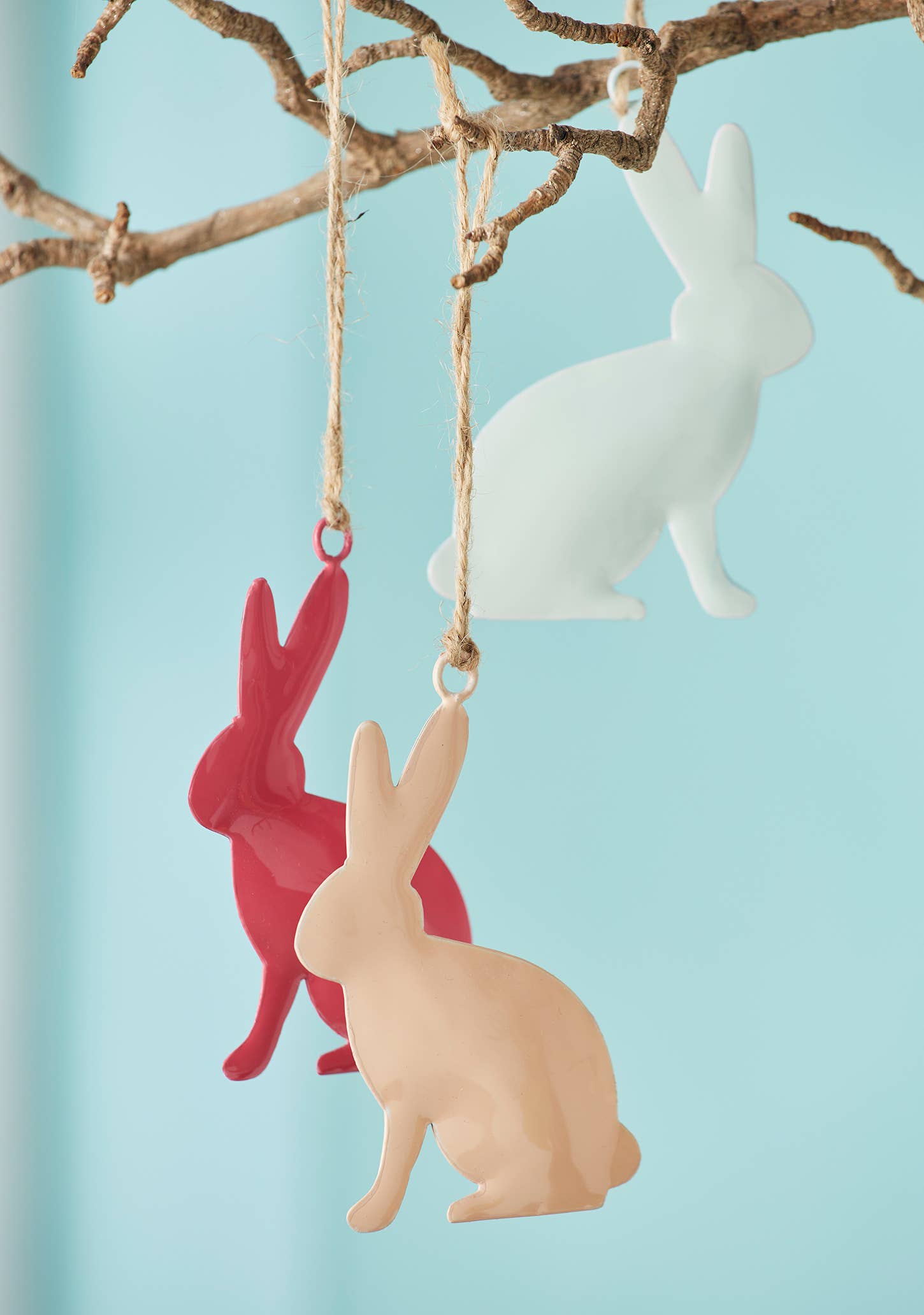 Decorative rabbit ornaments in red, beige, and white hanging from a branch against a light blue background.