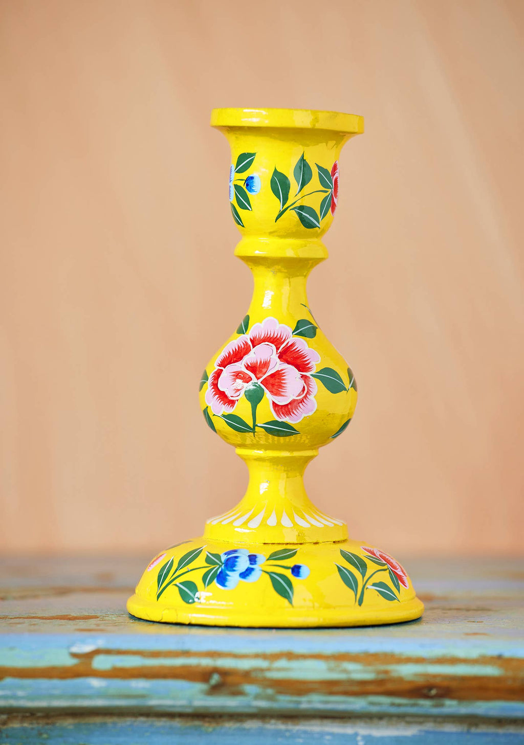 Yellow candle holder with floral designs on a wooden surface
