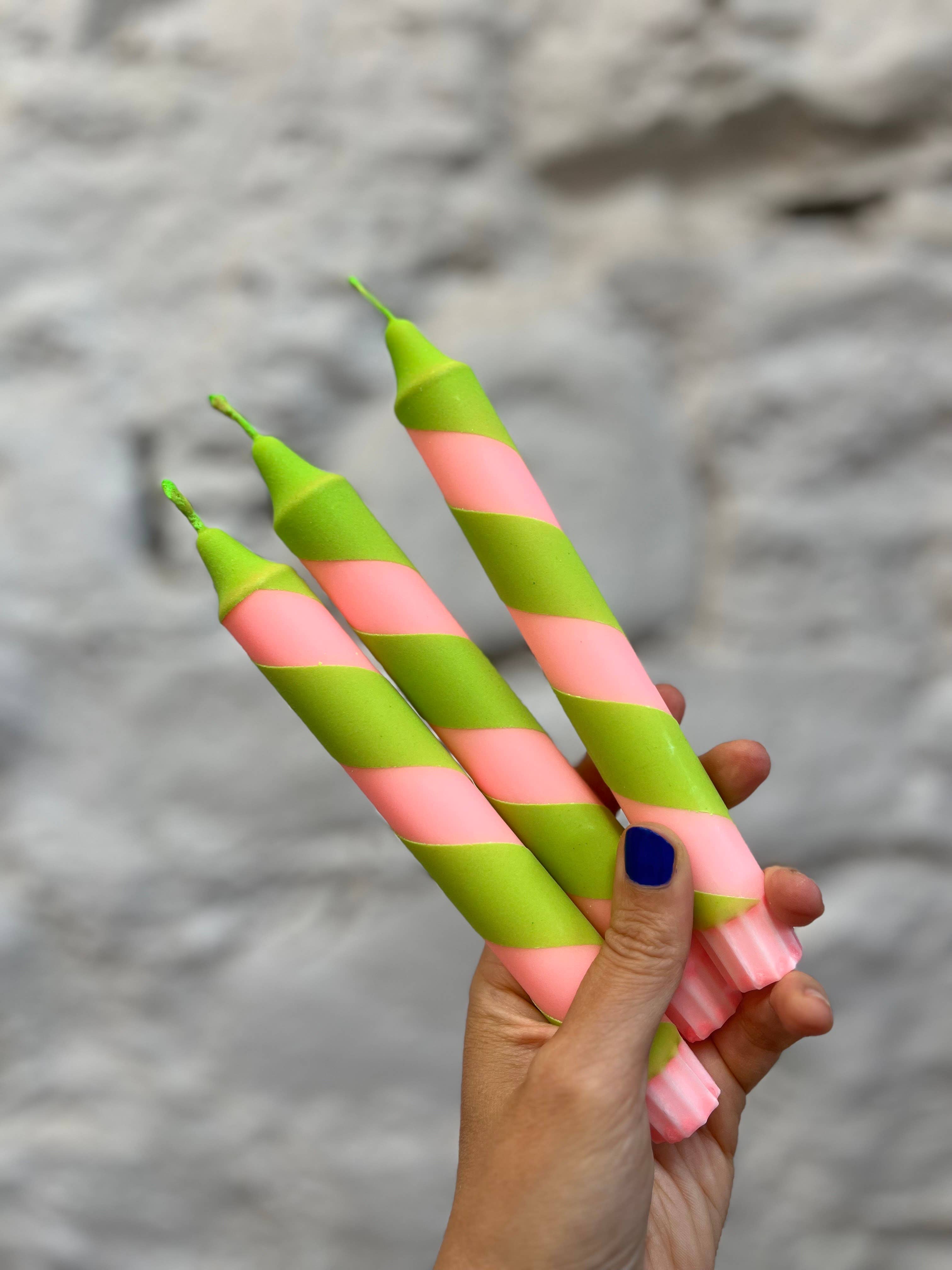 Hand holding three pink and green striped candles against a stone wall background