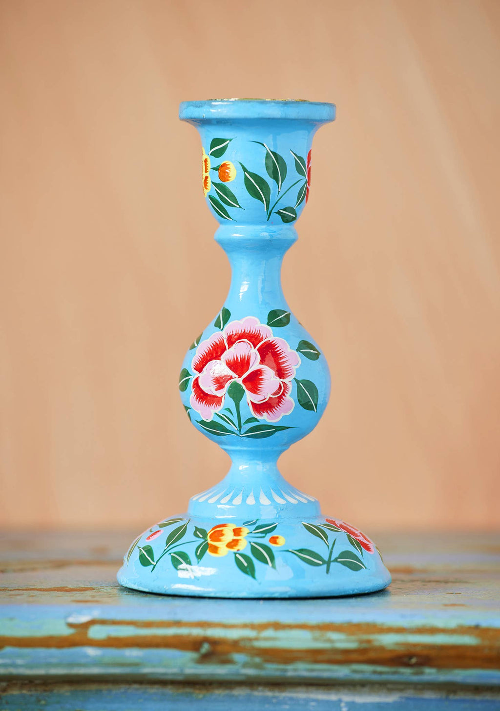 Blue candle holder with floral designs on a wooden surface