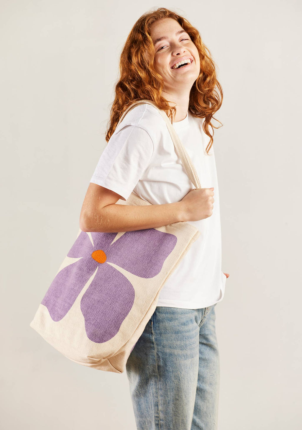 Person holding a tote bag with a purple flower design on a plain background